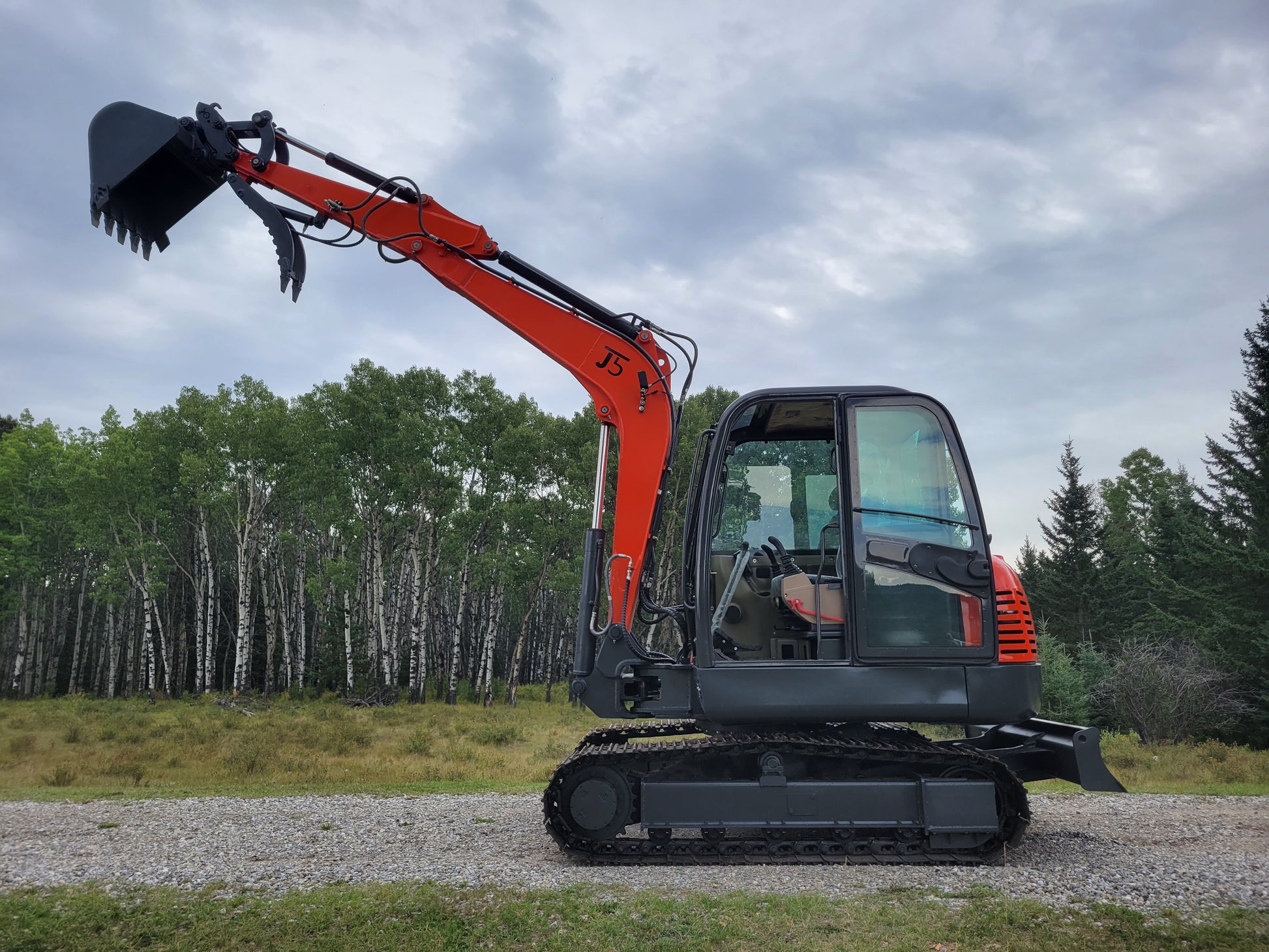 JT5600 mini excavator upright side profile with raised boom and bucket, showing clear operator cabin and rubber tracks in outdoor environment