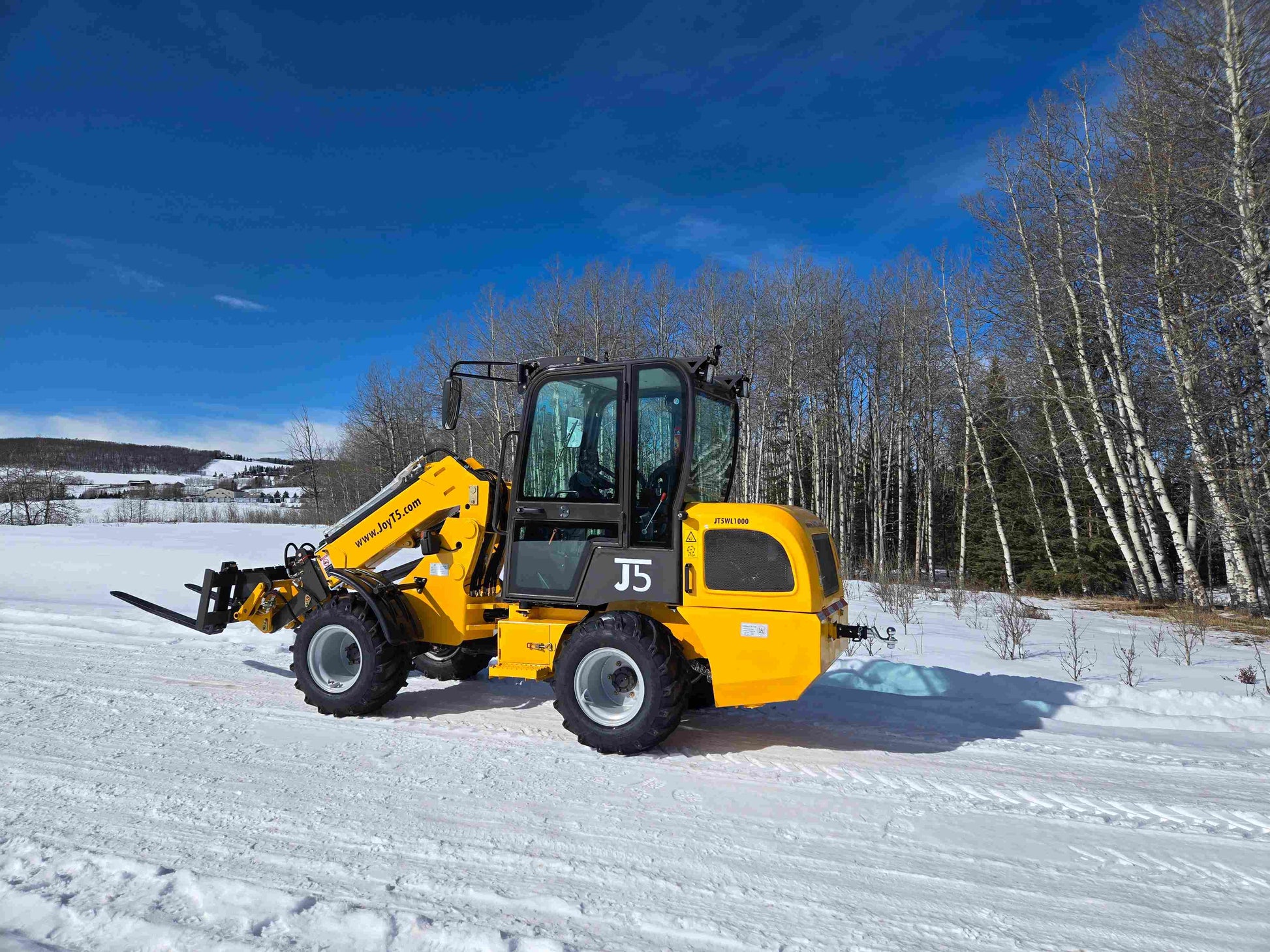 JT5WL1000 1 ton compact wheel loader lifting pallet forks on snowy job site in Canada for farm and construction material handling