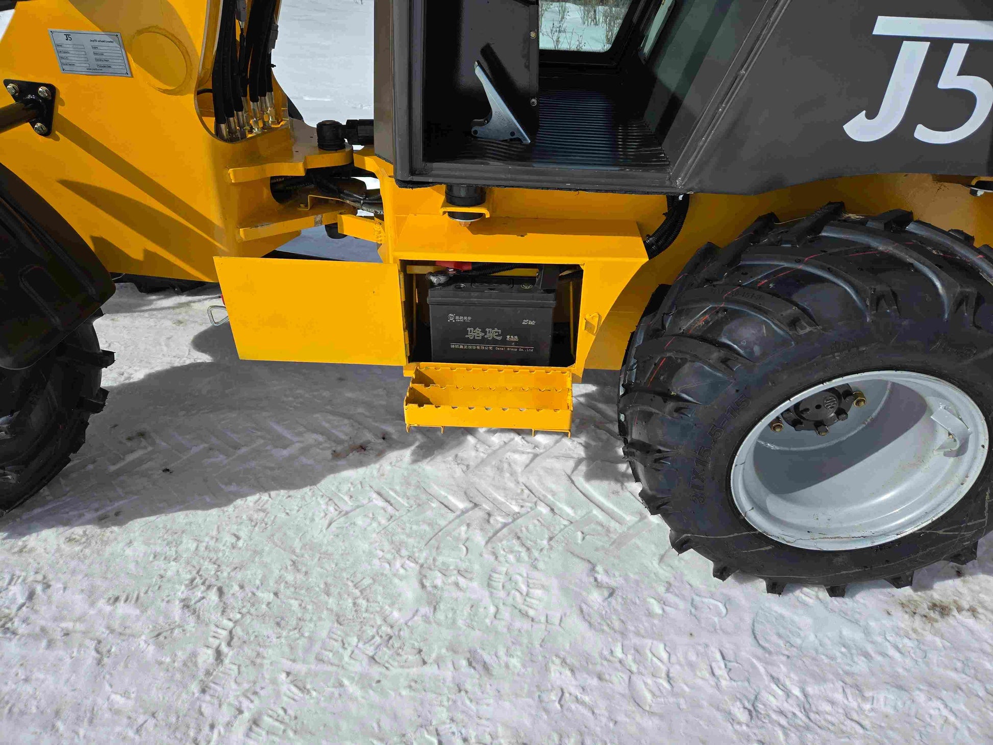 JT5WL1000 compact wheel loader battery compartment showcased in snowy Canada for farm landscaping and construction use