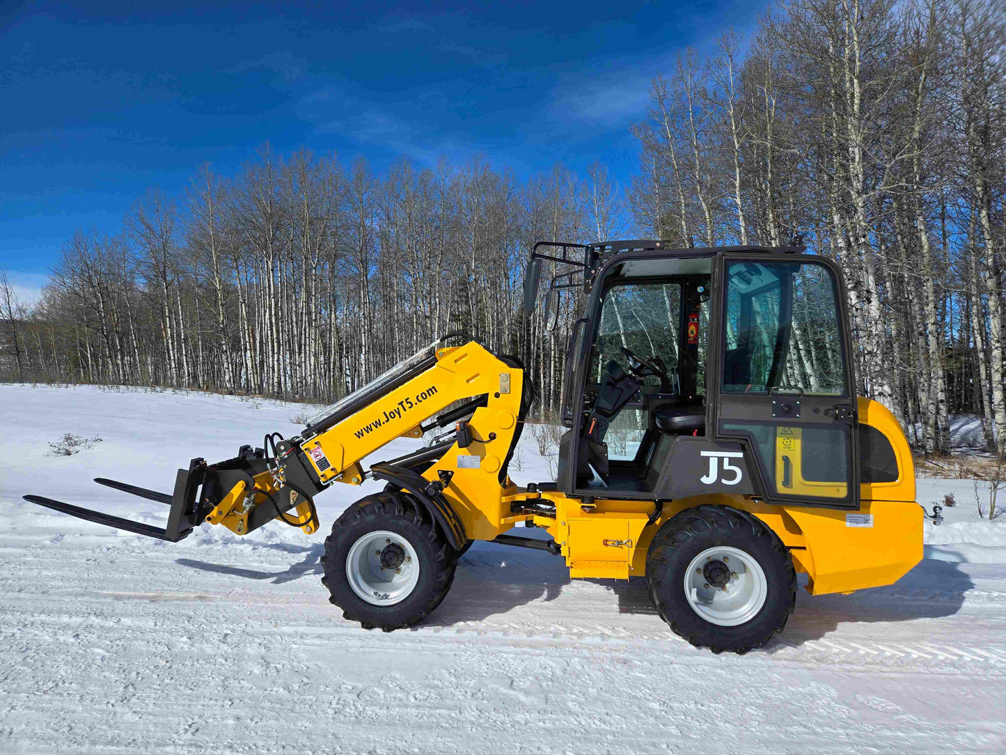 JT5WL1000 compact wheel loader with pallet fork attachment operating on snow in Canada for farm and construction lifting tasks