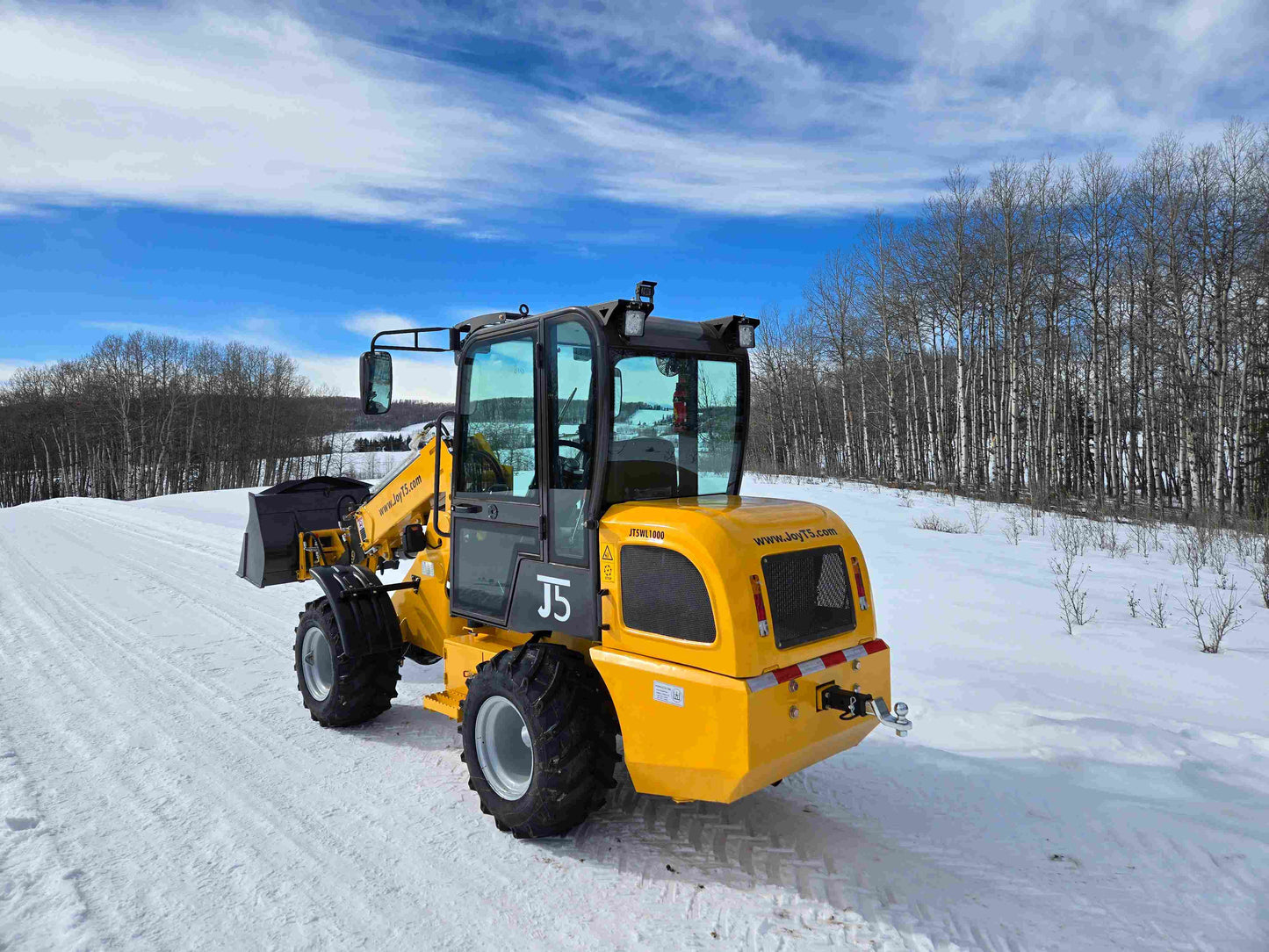 JT5WL1000 compact wheel loader lifting pallet forks in snowy landscape for farm and construction use in Canada