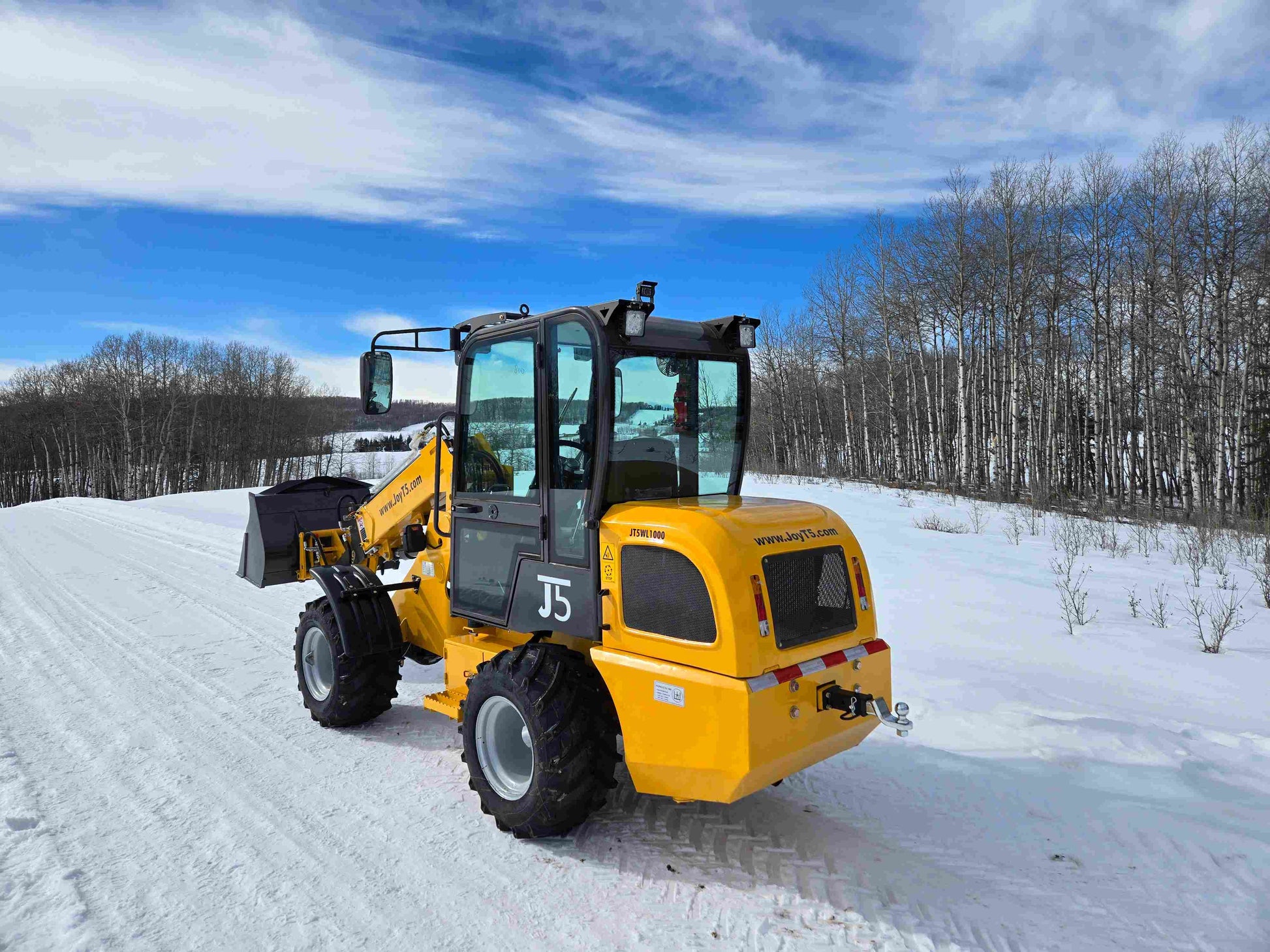 JT5WL1000 compact wheel loader lifting pallet forks in snowy landscape for farm and construction use in Canada