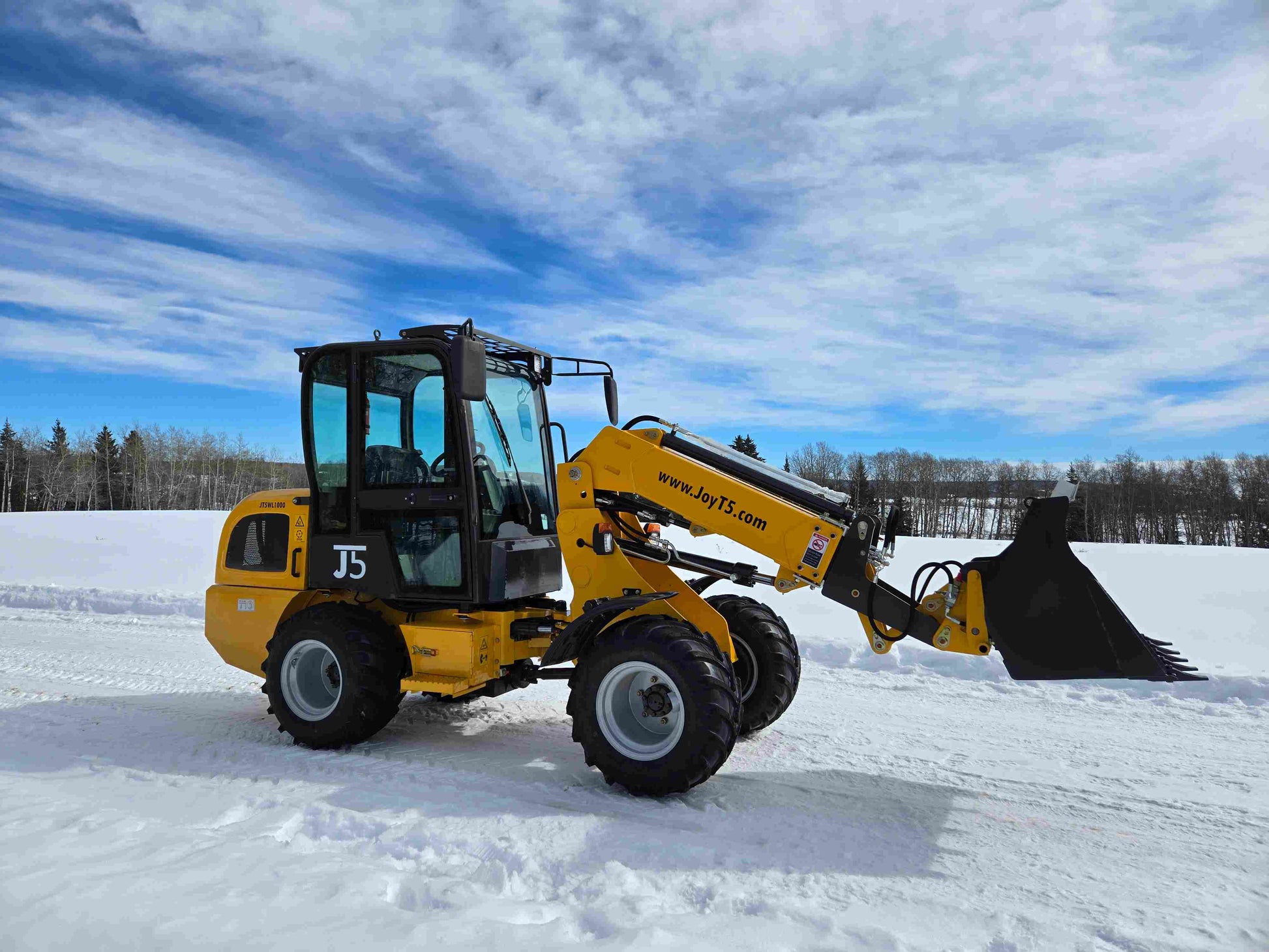 JT5WL1000 compact wheel loader operating with bucket in snowy construction and farm landscape in Canada