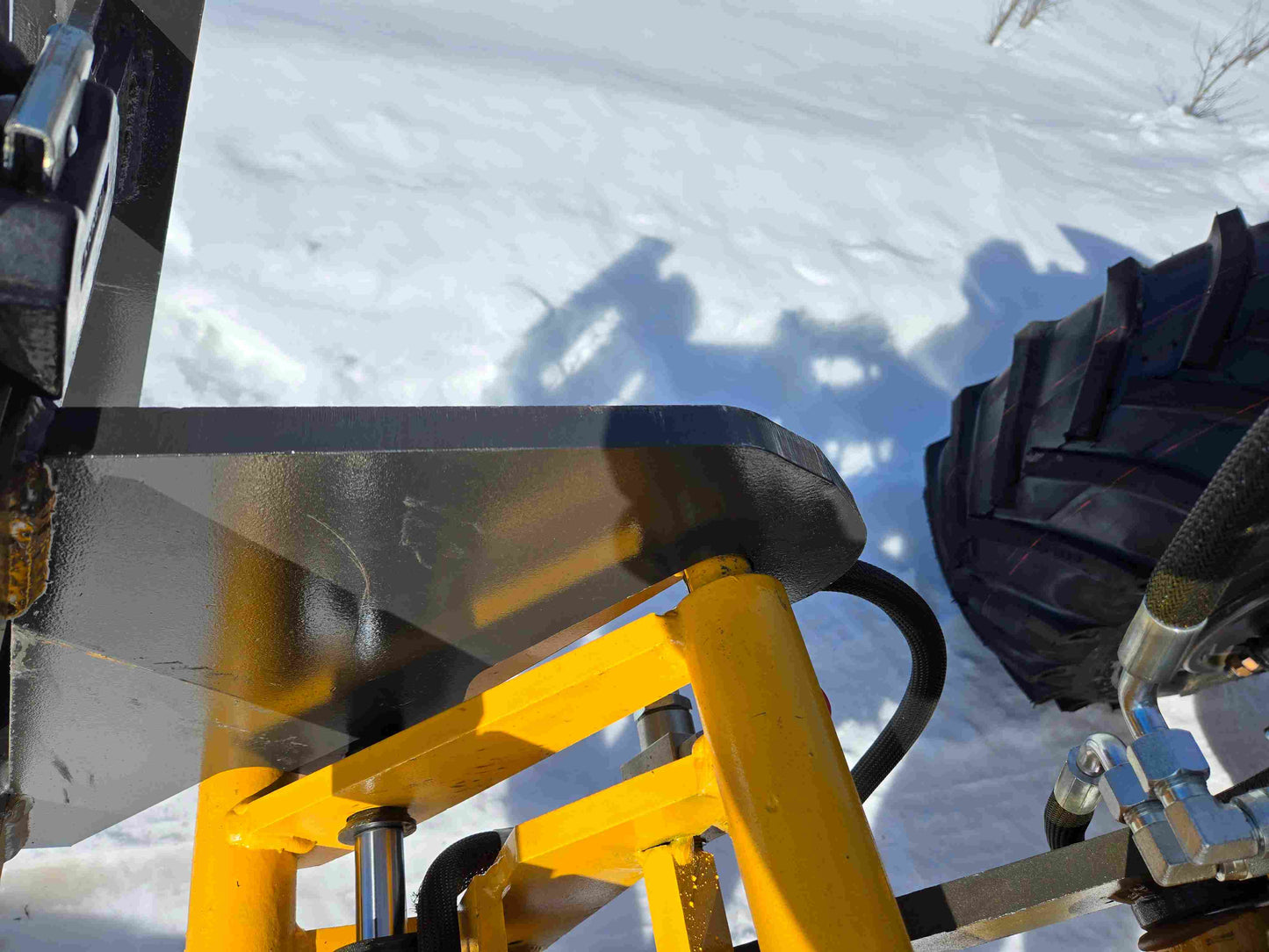 Close up view of JT5WL1000 compact wheel loader fork attachment showing hydraulic system details on snowy job site in Canada for farm and construction use