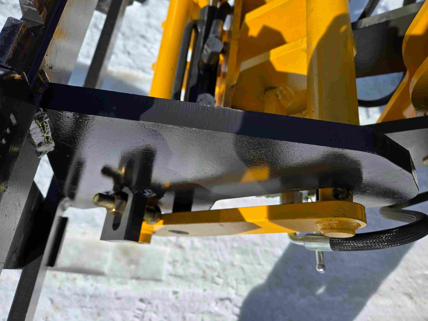 Hydraulic fork attachment mount of the JT5WL1000 compact wheel loader shown in detail on snow for material handling in Canada