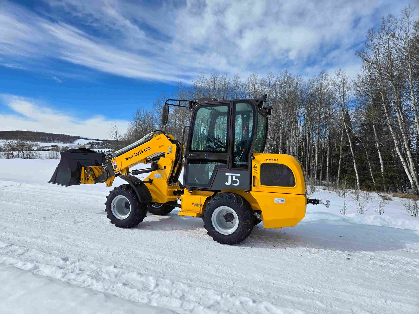 JT5WL1000 compact wheel loader lifting pallet forks on snowy jobsite in Canada for farm and construction material handling