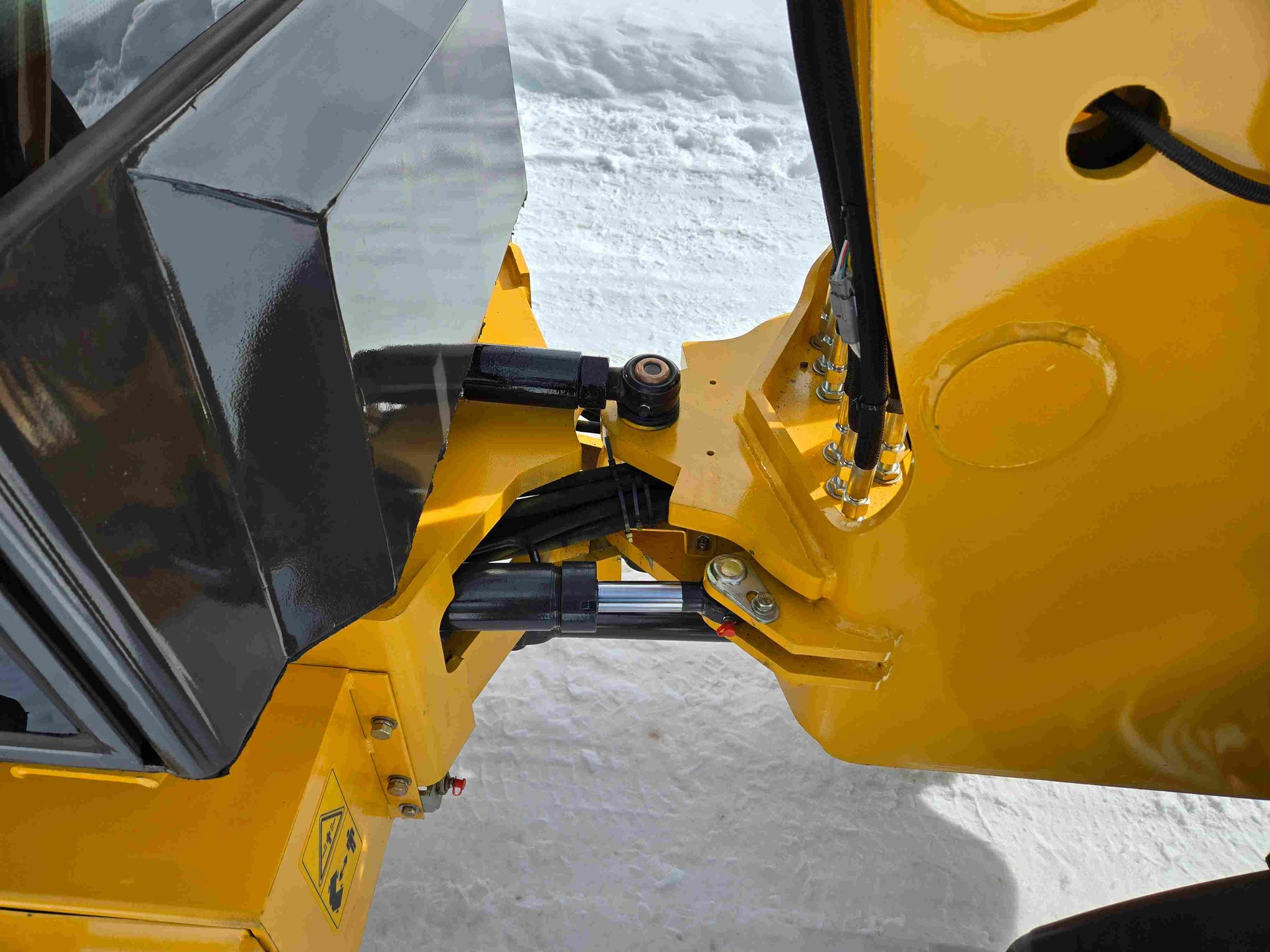 JT5WL1000 wheel loader central hinge joint with hydraulic cylinder and hose connections on snowy ground.