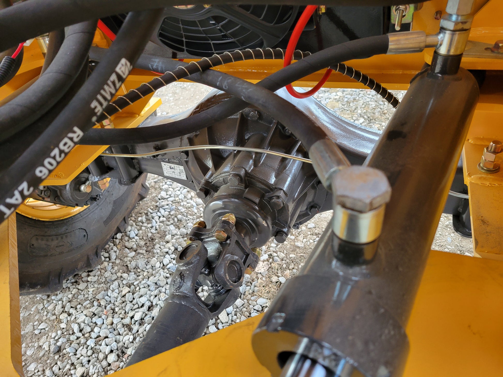 JT5WL1000 compact wheel loader showing close-up of front axle, hydraulic steering cylinder, and drive shaft components.