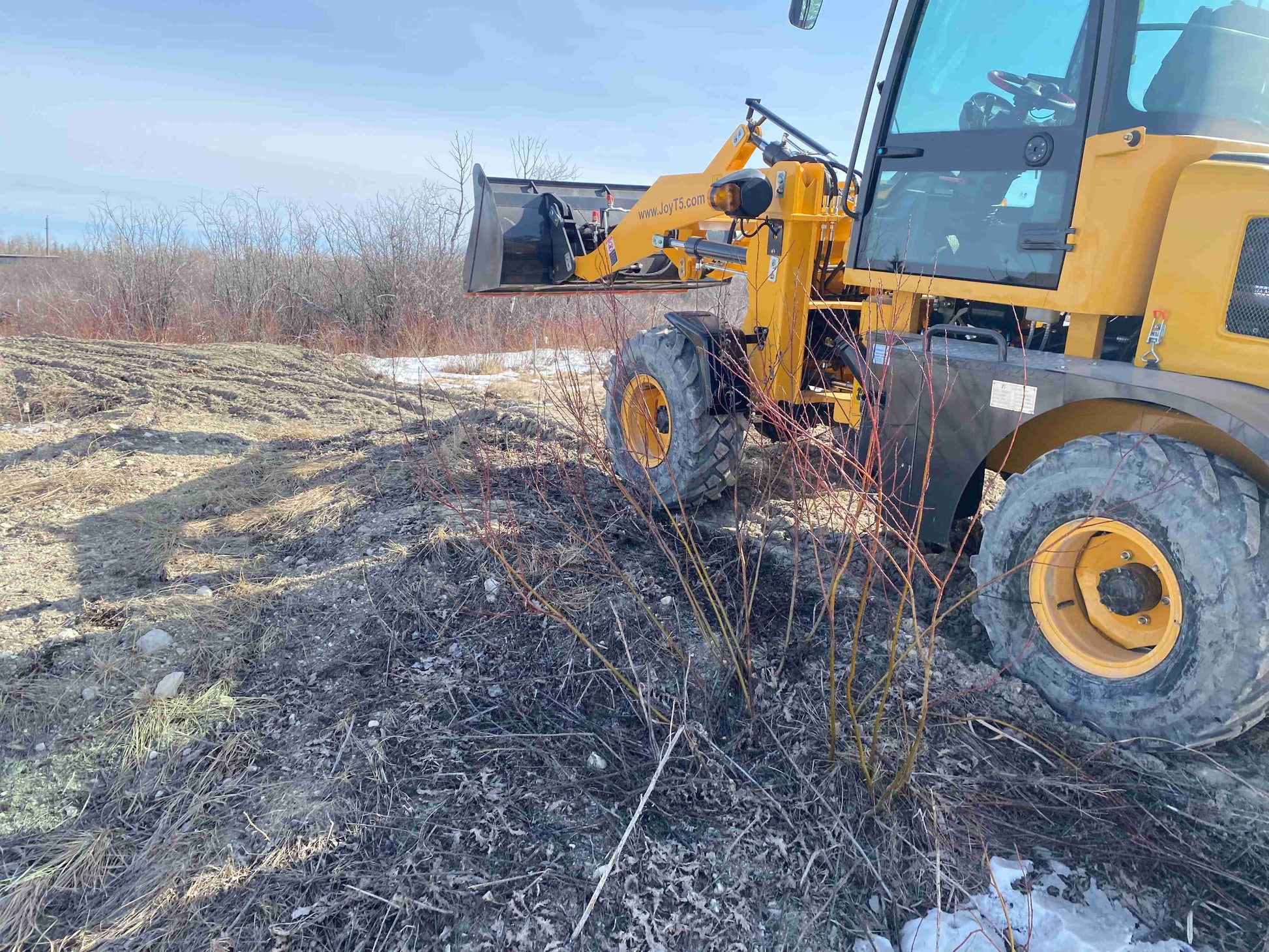 JT5WL1200 compact wheel loader with front bucket operating on rough terrain - small construction loader for farming and landscaping work