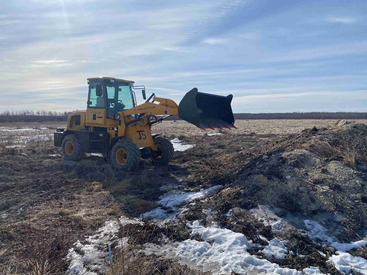JT5WL1200 compact wheel loader lifting soil with front bucket during construction work and landscaping in Canada