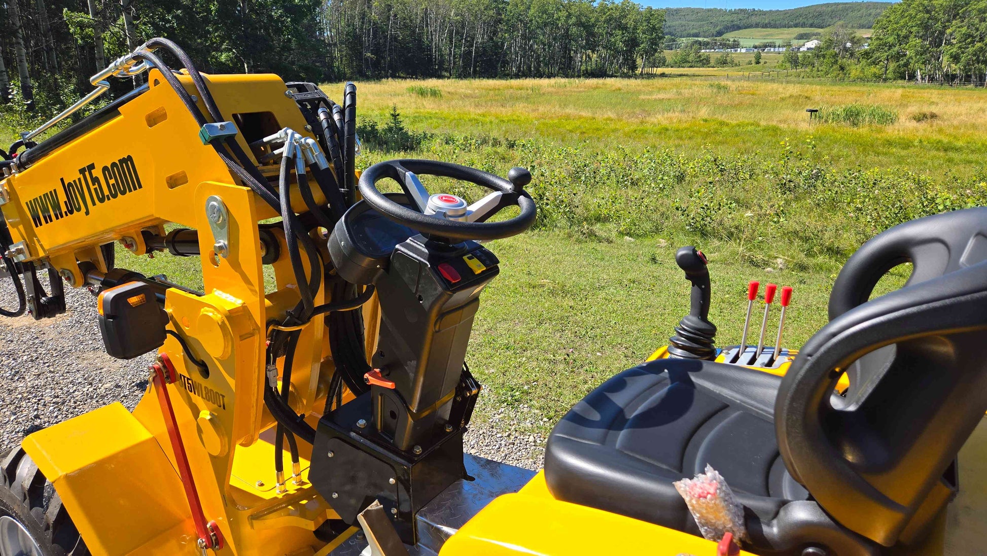 Operator seat steering wheel and control levers of the JT5WL800 compact wheel loader shown in an open field ready for farm landscaping and construction work in Canada