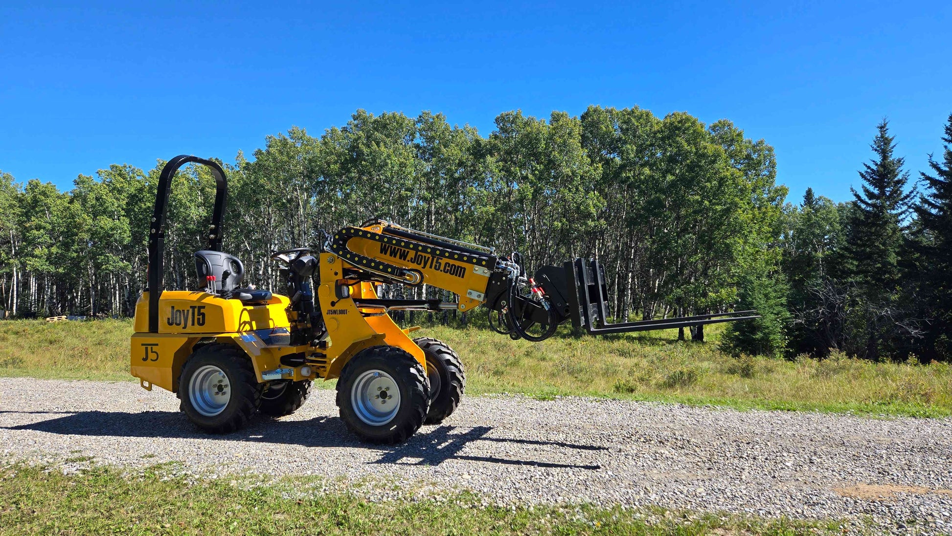 JT5WL800 mini wheel loader with fork attachment side view lifting forks extended on gravel road with trees background