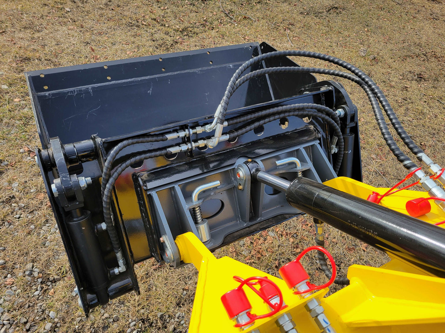 Close-up of a JoyT5 mini skid steer hydraulic bucket attachment with hoses and locking pins.