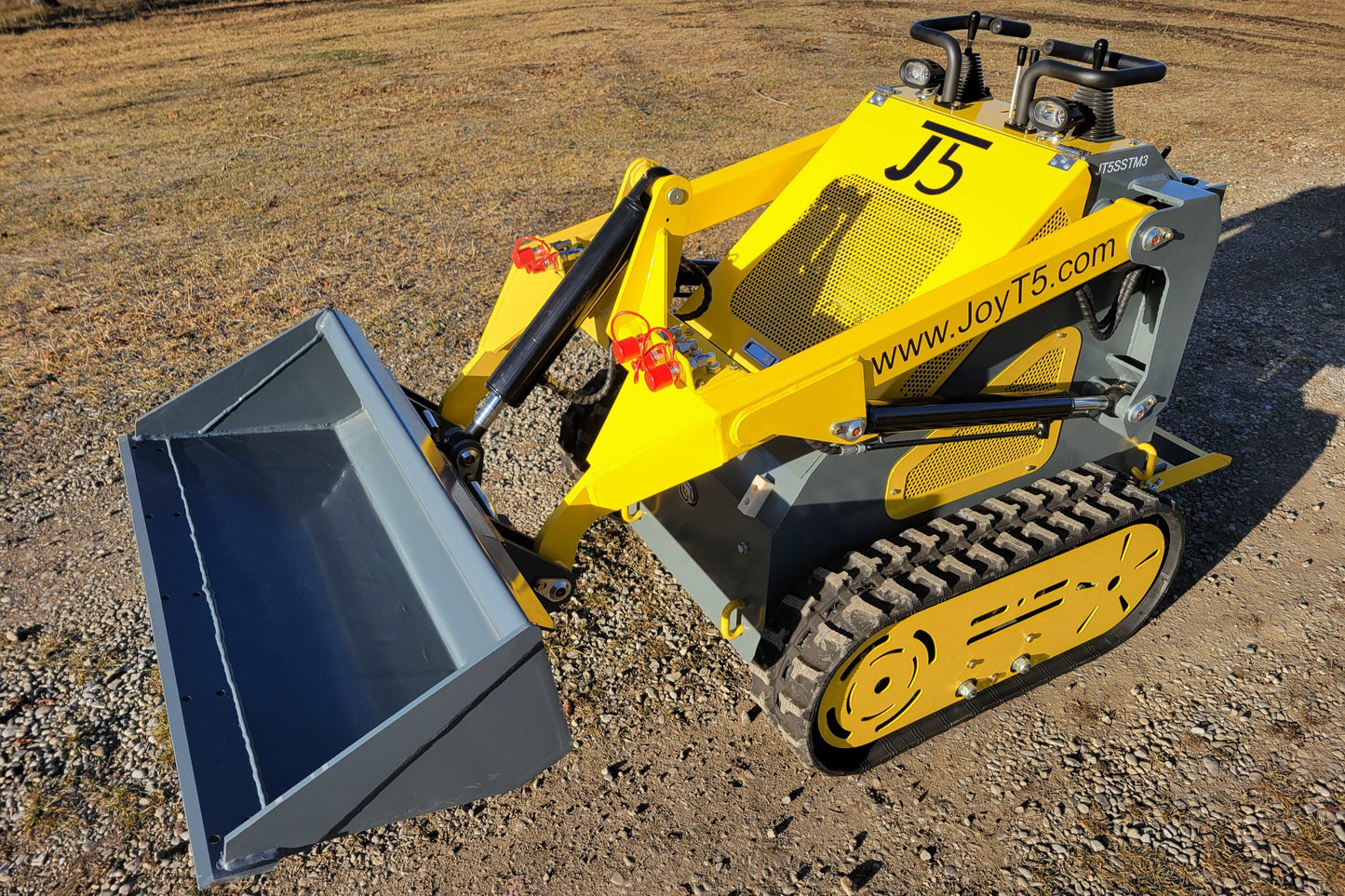 Yellow mini tracked skid steer loader with front bucket attachment parked on gravel surface in Canada used for landscaping agriculture and construction

