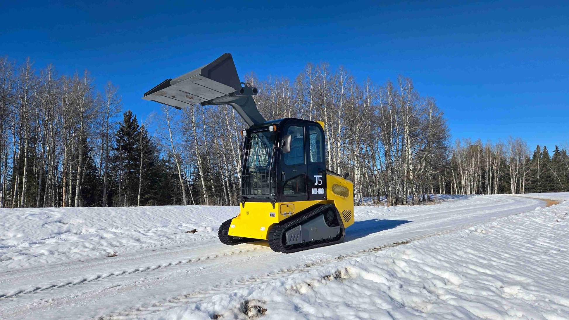 Rippa NDI680 skid steer loader with 74 HP engine and raised bucket operating on snowy road in Alberta Canada | JoyT5