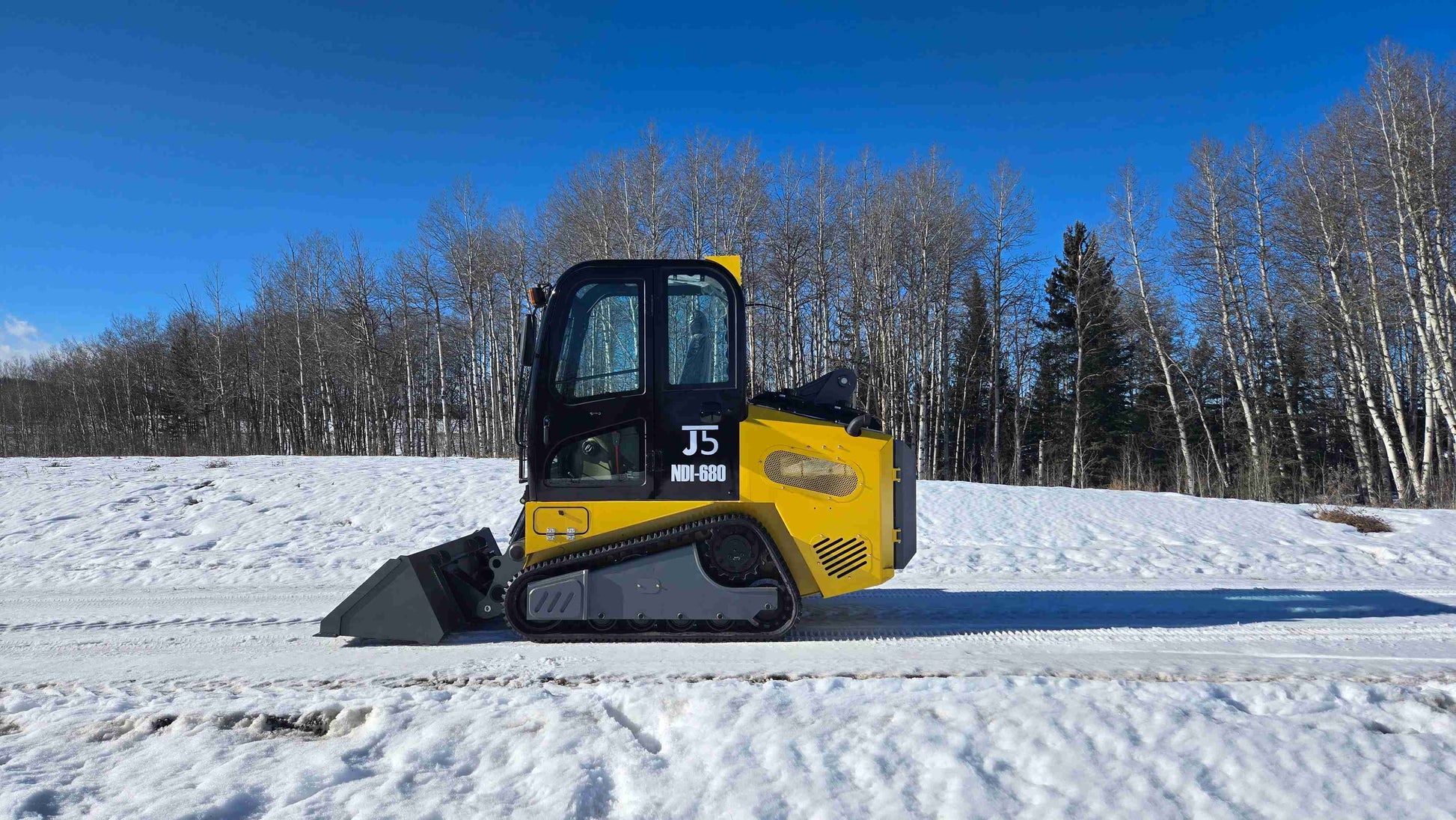 Side view of Rippa NDI680 compact skid steer loader with 74 HP engine and 1250kg lift capacity on snowy job site in Alberta Canada | JoyT5