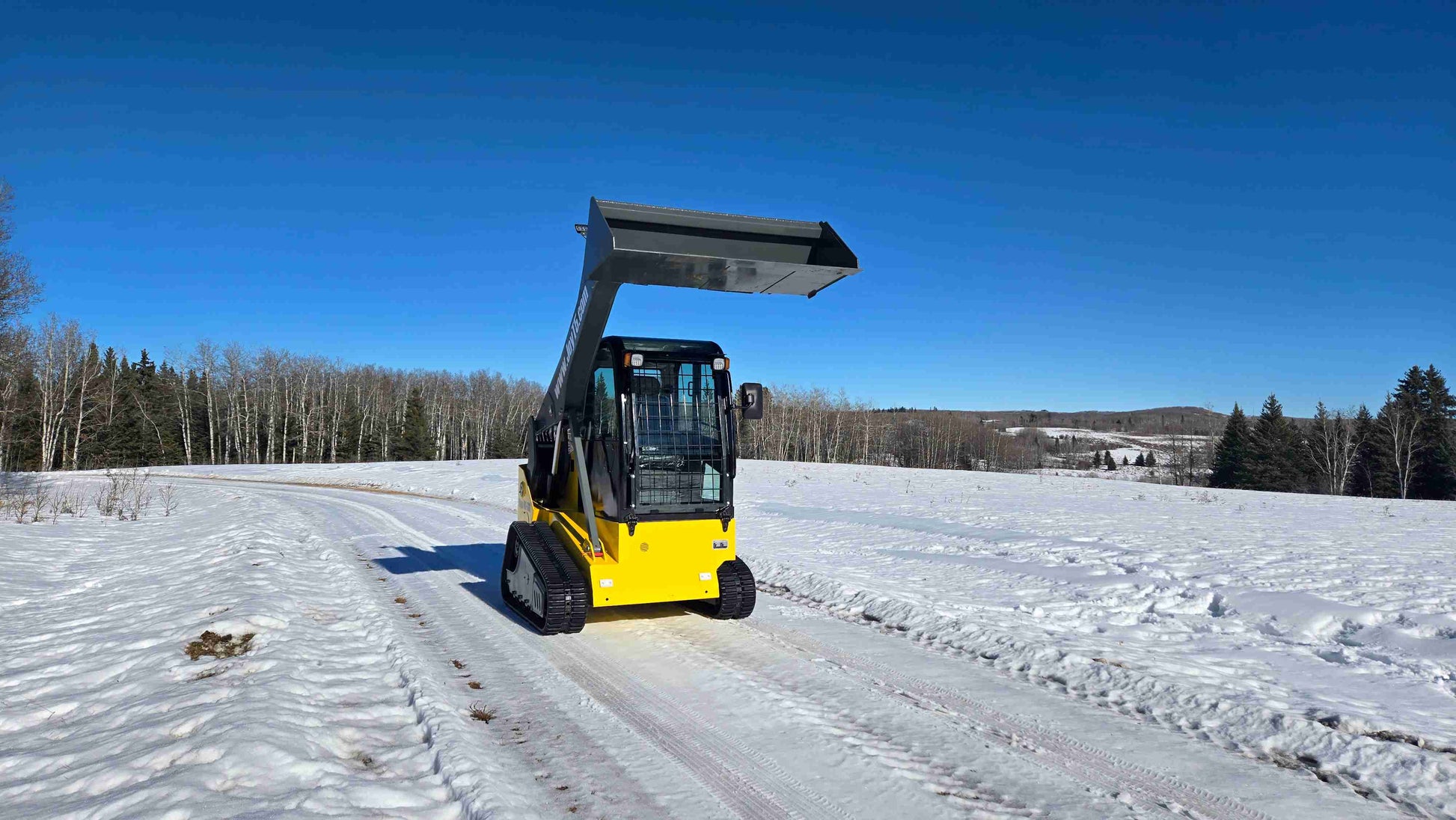 Front view of Rippa NDI680 compact skid steer loader with elevated bucket on snowy construction site in Canada | JoyT5