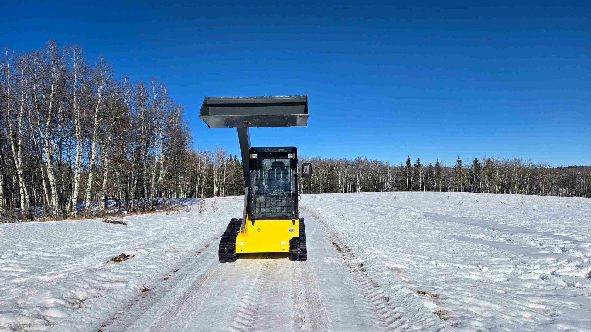 Front view of Rippa NDI680 compact skid steer loader with 74 HP engine and raised bucket on snowy trail in Canada | JoyT5