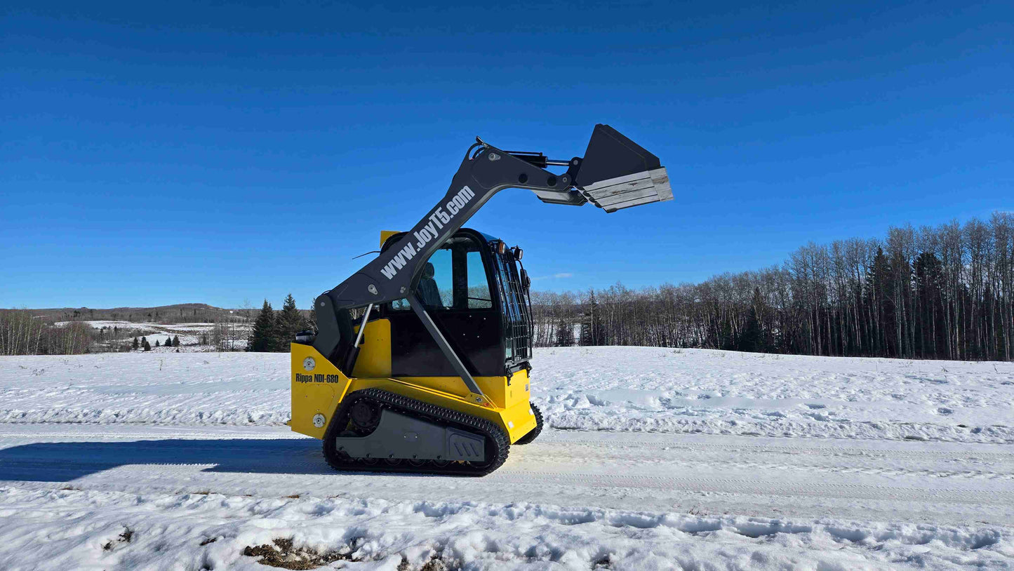 Side profile view of Rippa NDI680 compact skid steer loader with 74 HP engine and raised bucket on snowy field in Canada| JoyT5