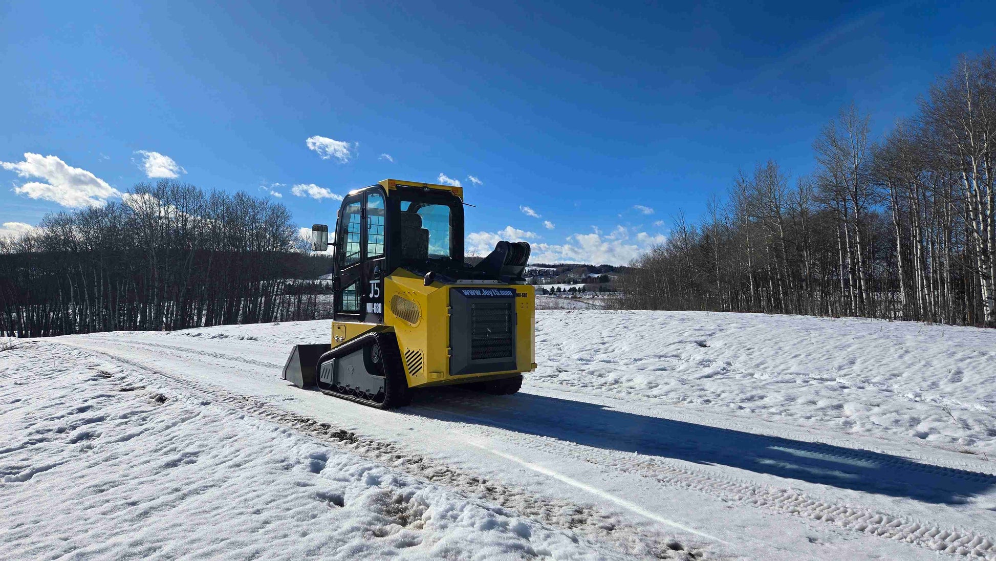 Side view of Rippa NDI680 skid steer loader 74 HP compact design with 1250kg lift operating on snow in Canada | JoyT5
