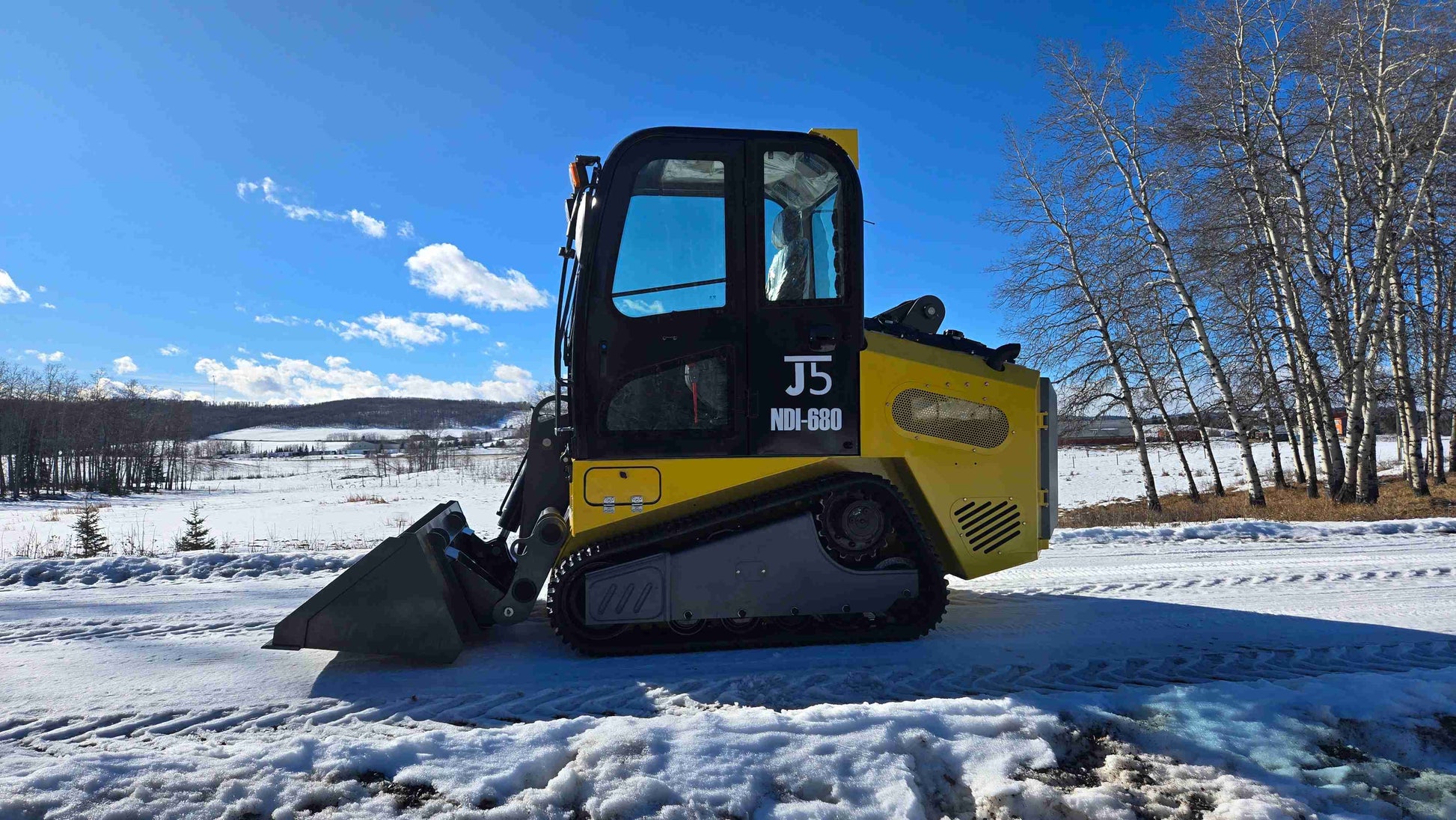 rippa NDI680 skid steer 74 HP compact tracked loader with bucket attachment operating on snowy field in Canada