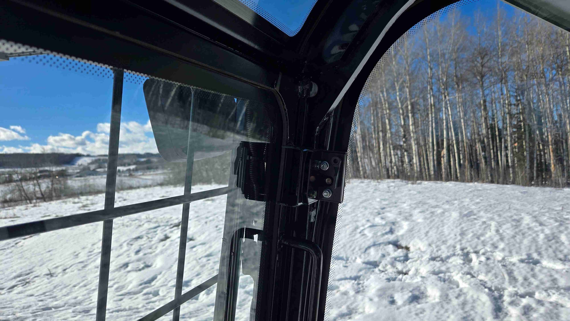 Inside view from the cab of Rippa NDI680 skid steer loader showing protective window grid and snowy landscape | JoyT5