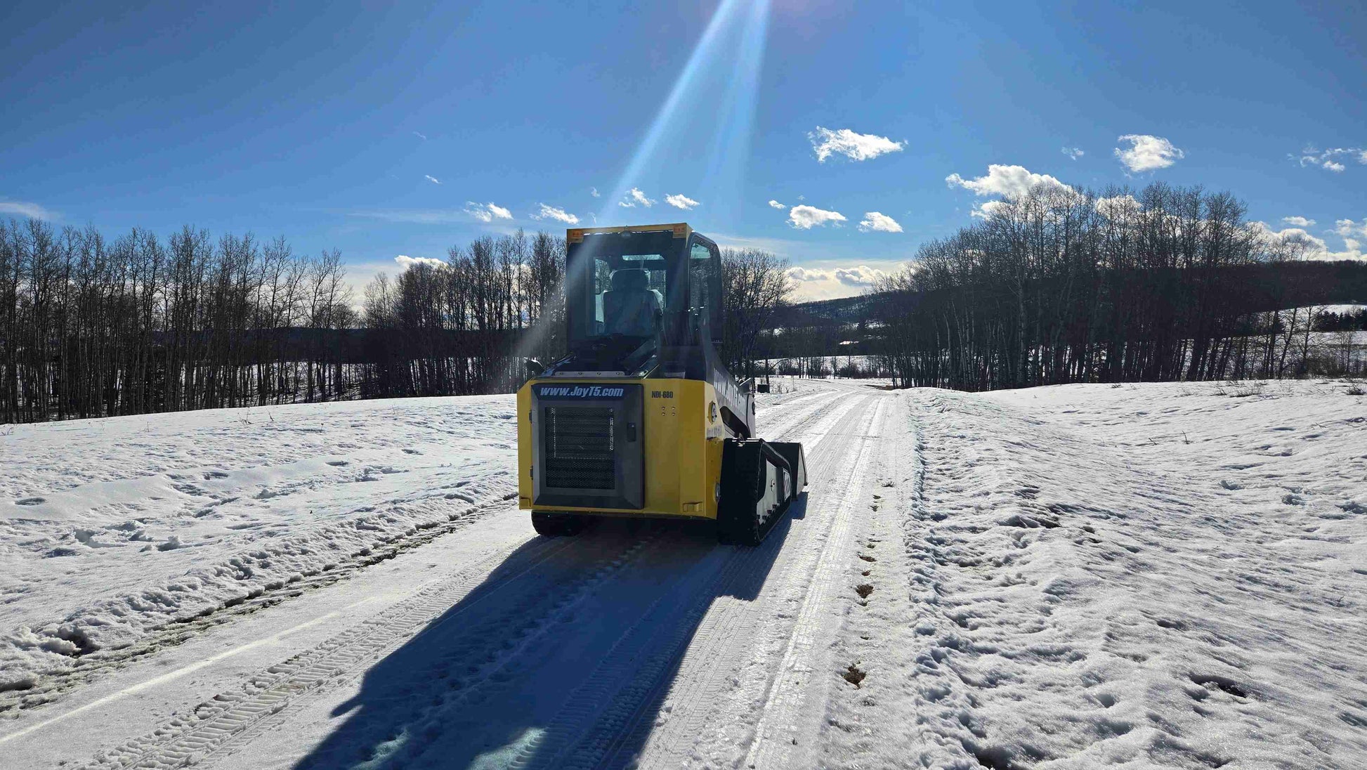Front view of Rippa NDI680 skid steer loader with 74 HP engine operating on snowy road in Alberta Canada | JoyT5