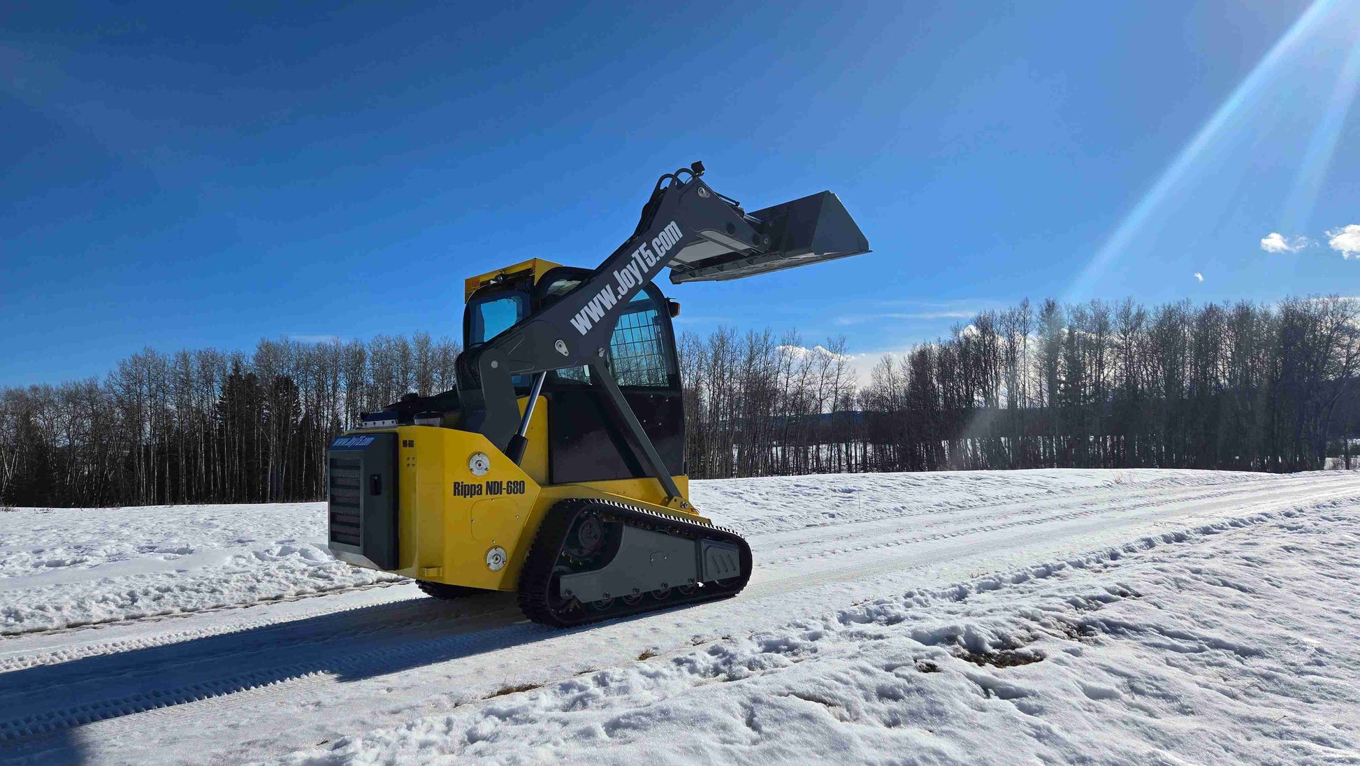 Rippa NDI680 skid steer loader rear-side angled view with raised bucket, compact tracked loader in snowy Canada| JoyT5