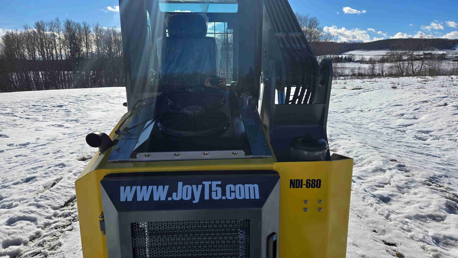 Rear view of Rippa NDI680 skid steer loader showing cooling fans, cabin interior, and JoyT5 branding on snowy terrain | JoyT5