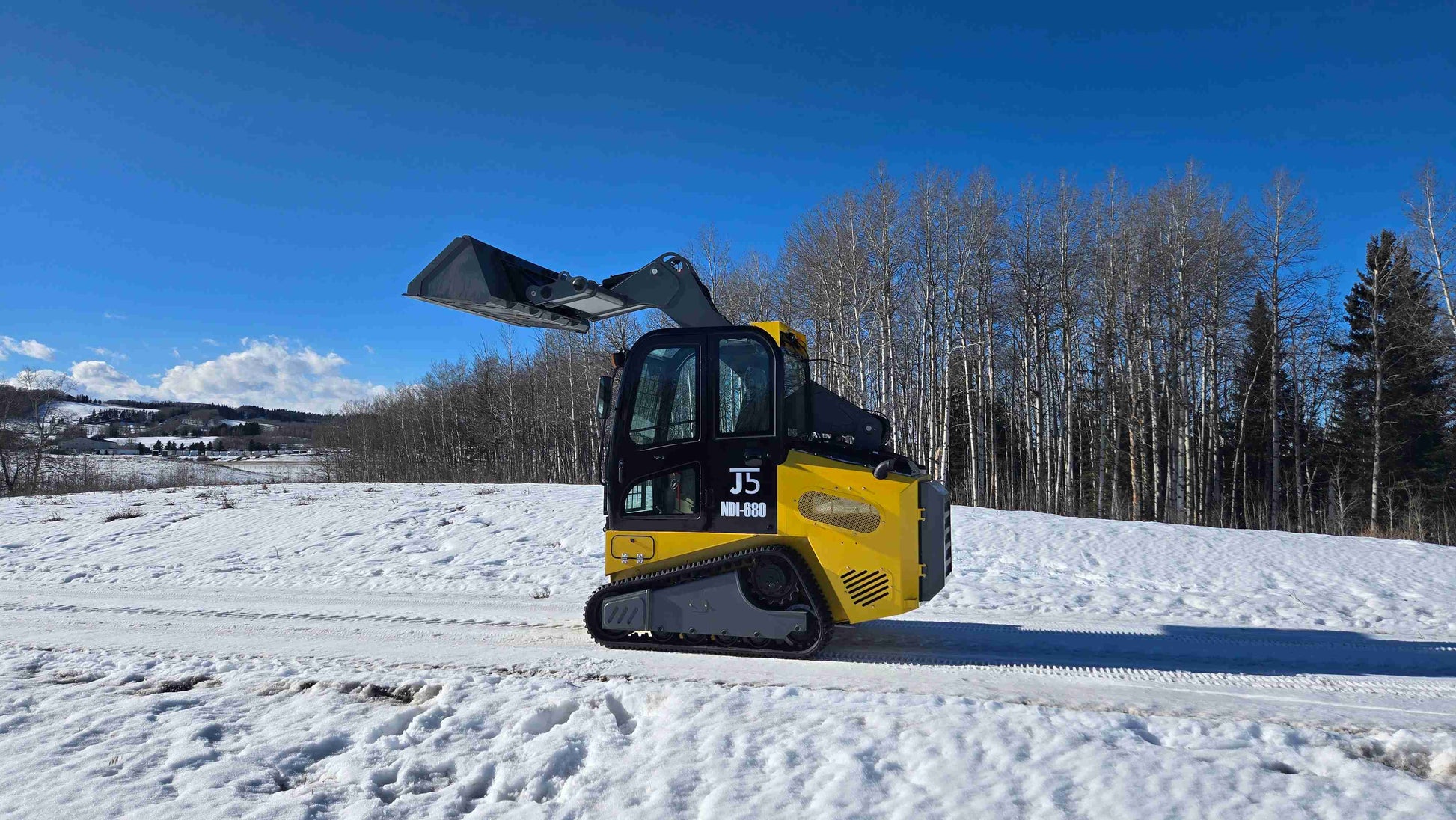 Rippa NDI680 skid steer side view with raised bucket operating on snowy road in Canada by JoyT5
