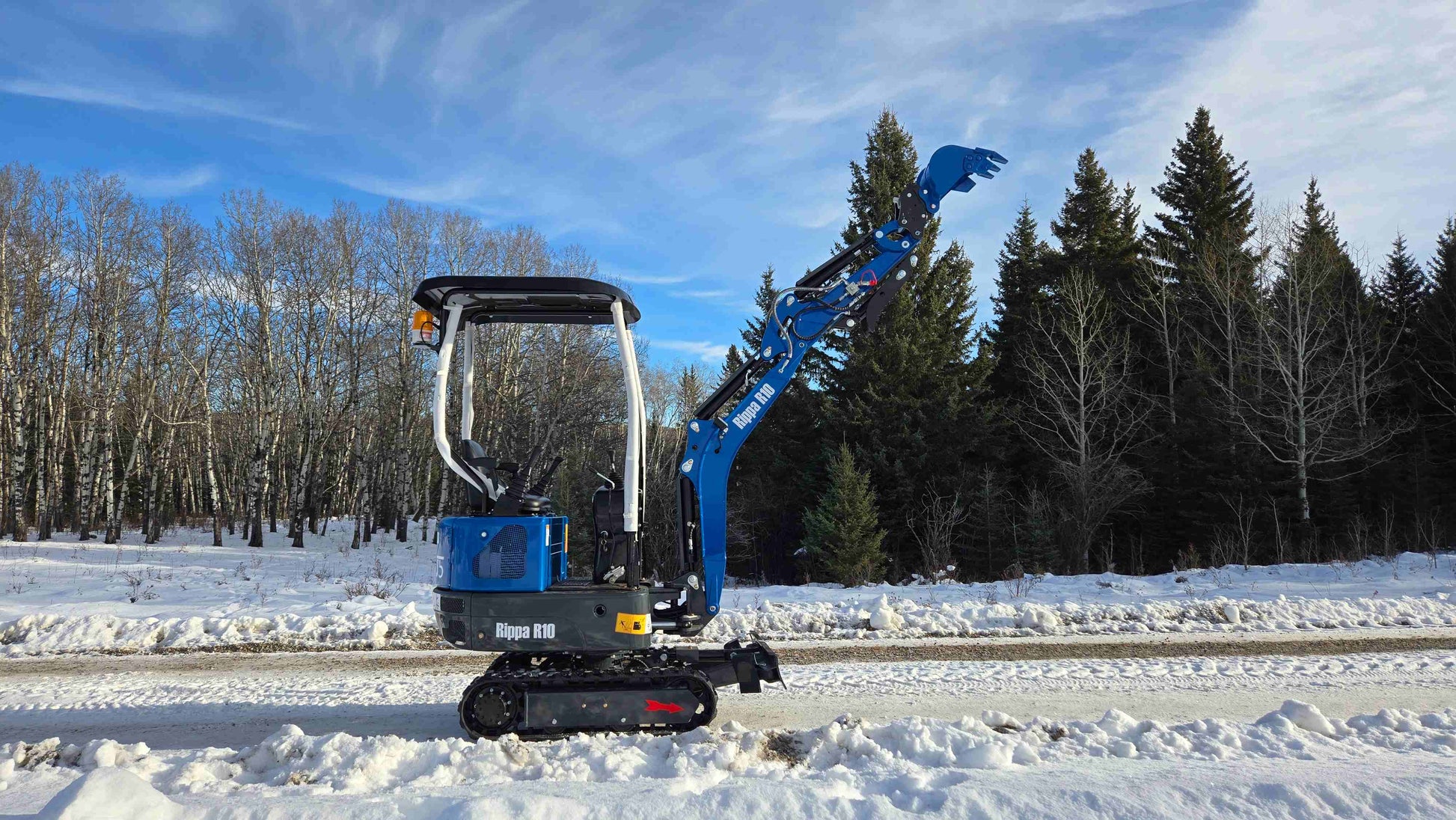 Side view of Rippa R10 mini excavator with boom arm lifted on snowy ground in Canada, compact and powerful construction digger by JoyT5 for tight space projects.