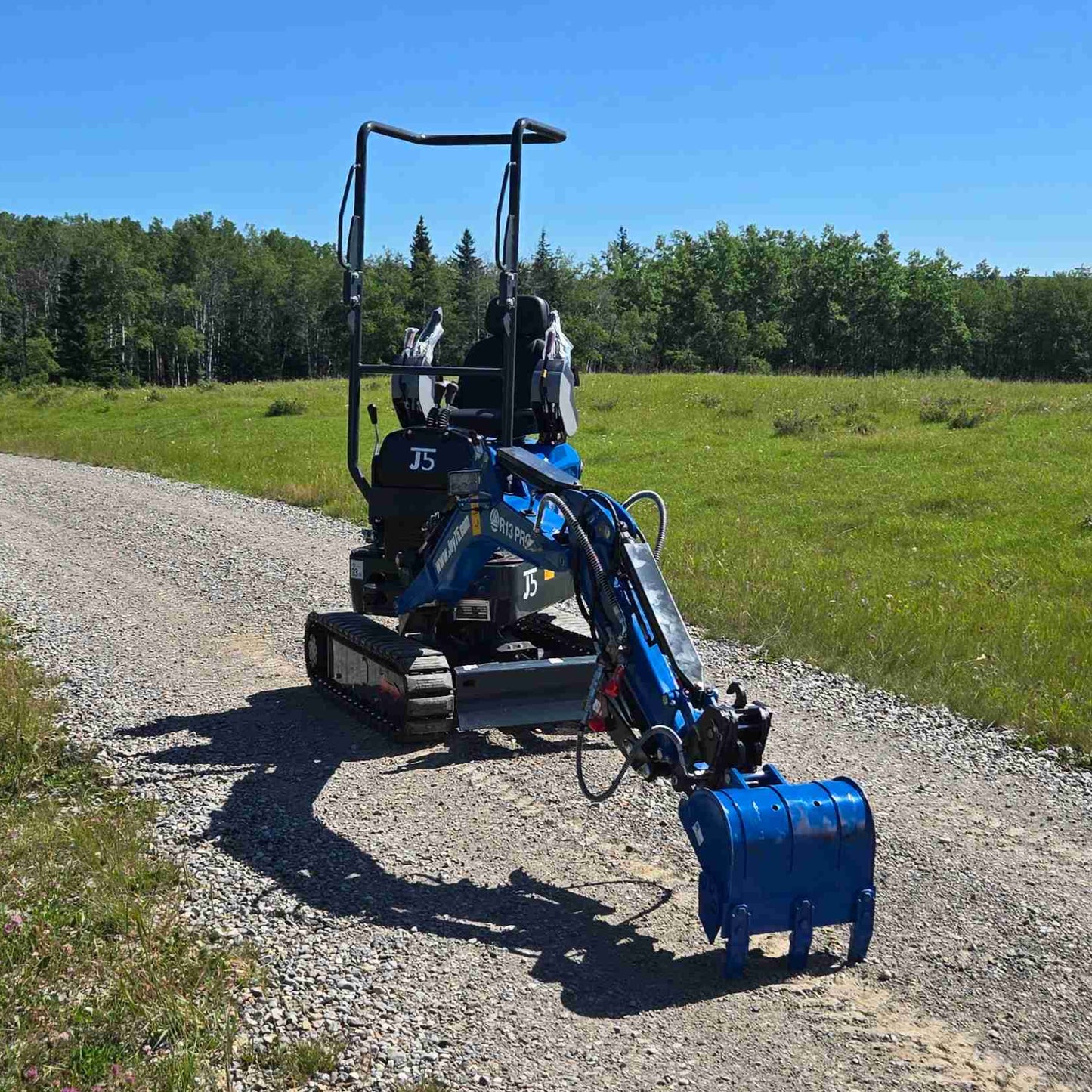 Rear side view of Rippa R13 1.3 ton mini excavator with extended arm and bucket on gravel road | Compact mini excavator for construction and landscaping work in Canada with JoyT5 support