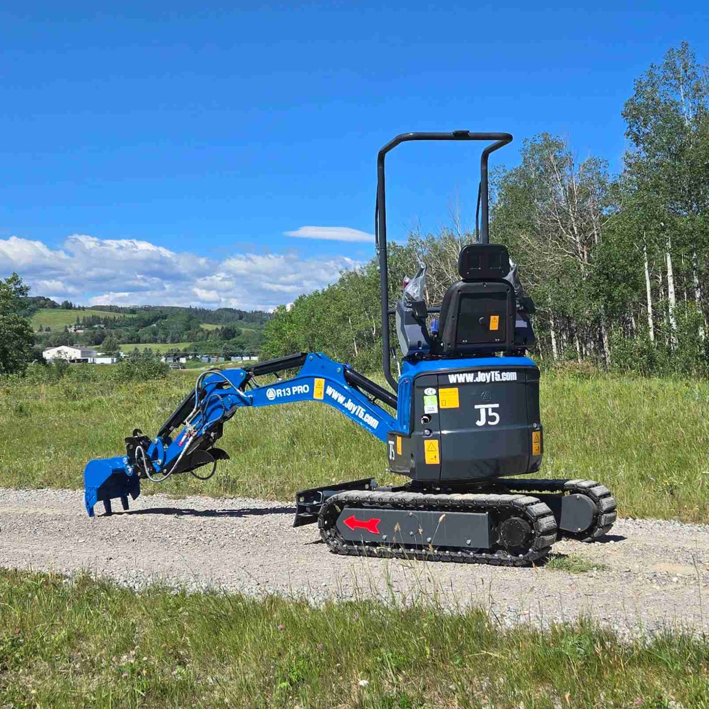 Rear side view of Rippa R13 1.3 ton mini excavator with boom extended, showing compact tracked design and operator seat on gravel road | Small mini excavator for landscaping, trenching, and construction work in Canada with JoyT5 support
