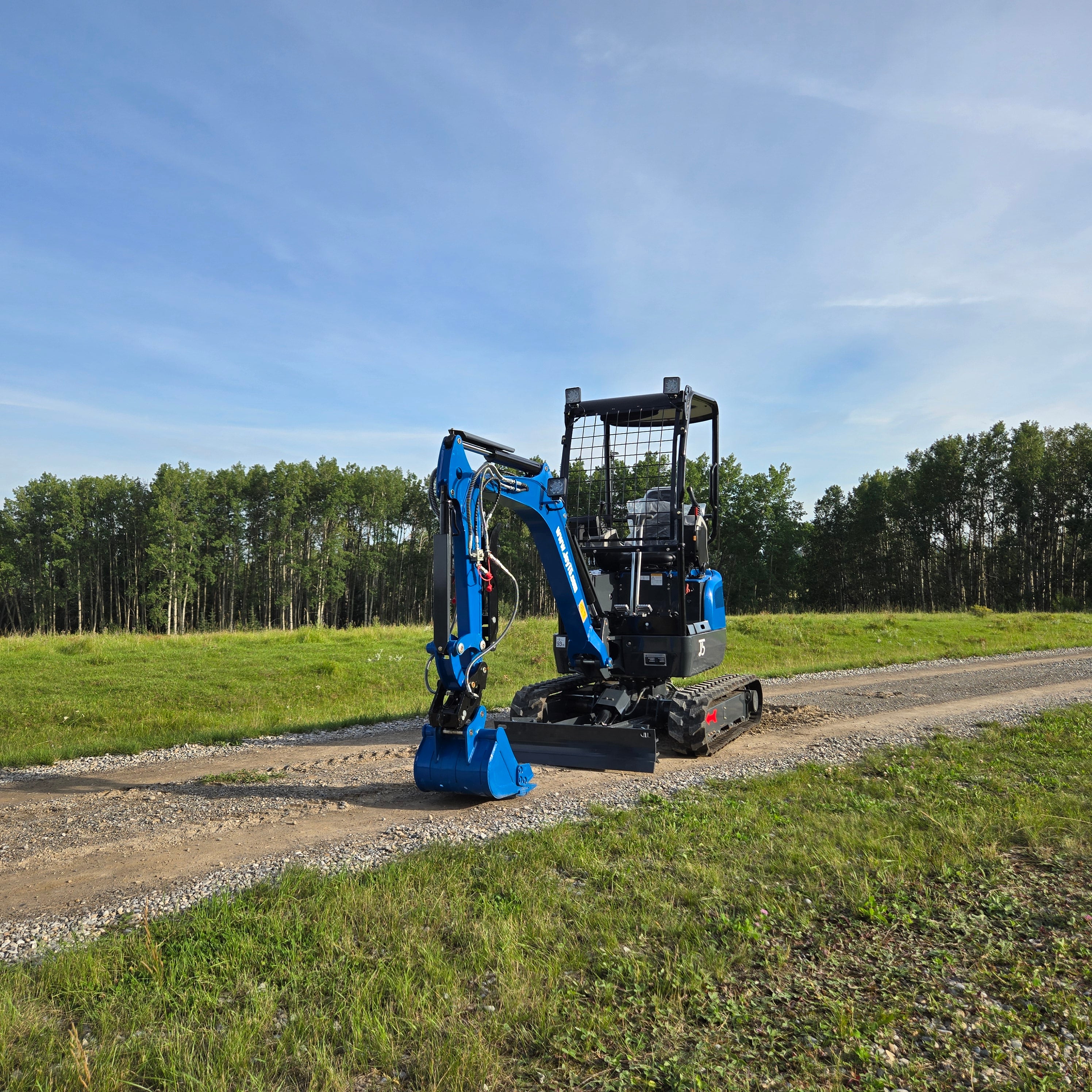 Front side view of Rippa R18- Mini Excavator working on a gravel road with green grass and trees in the background.