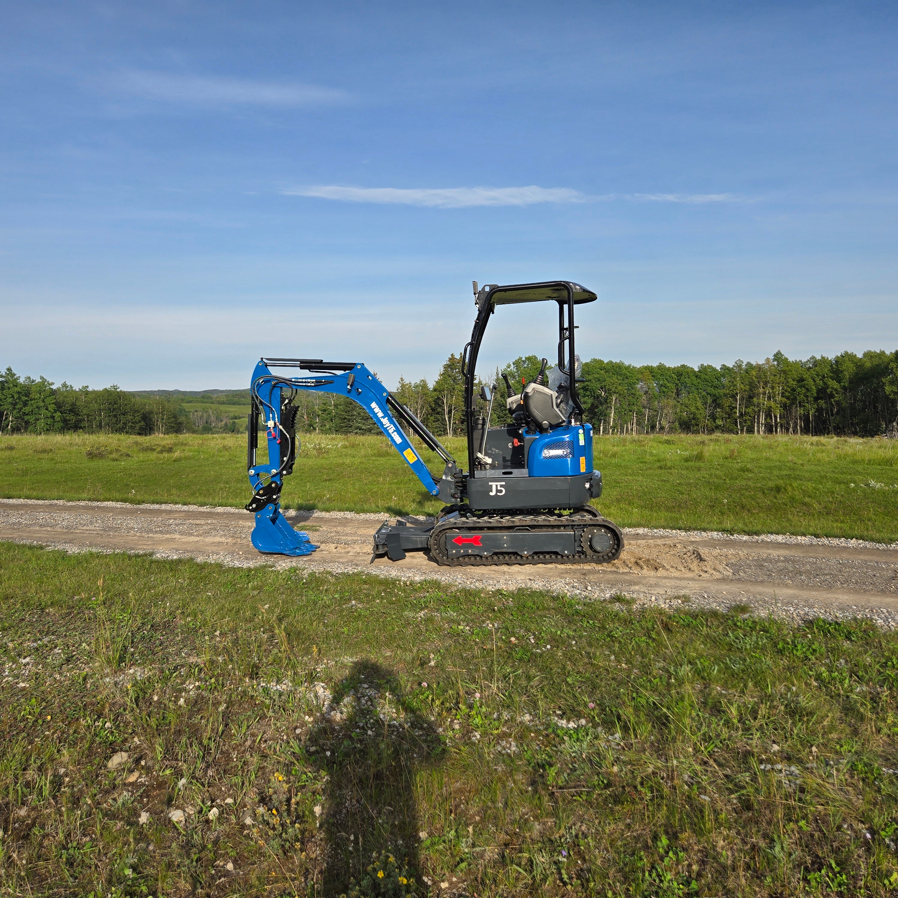 Rippa R18- Mini Excavator side view on a construction site with blue sky and green field.