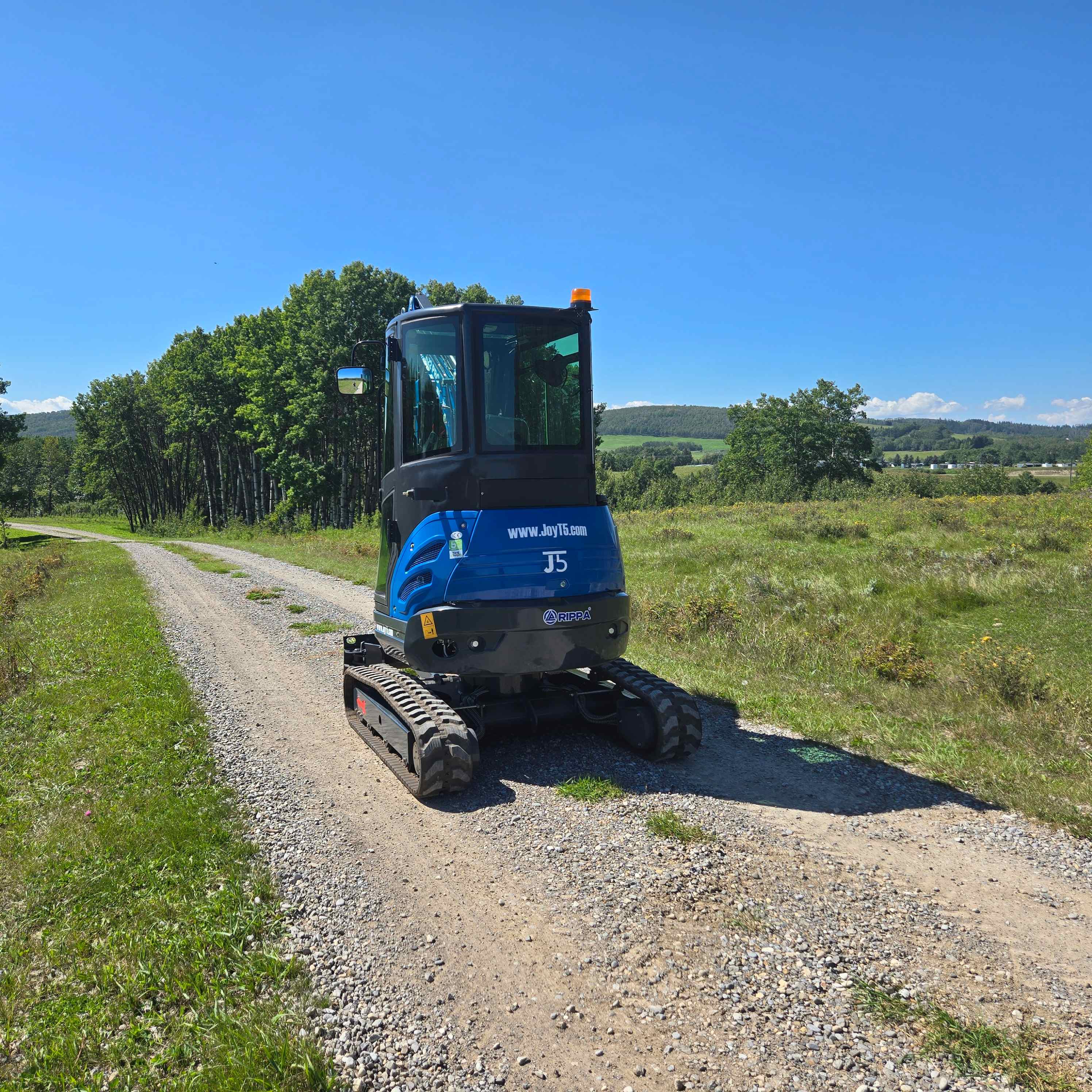 Rippa R22 2 ton mini excavator for sale in Canada parked on a rural gravel road with fields and trees, compact Yanmar engine digger designed for construction and landscaping projects, available from JoyT5 in Canada