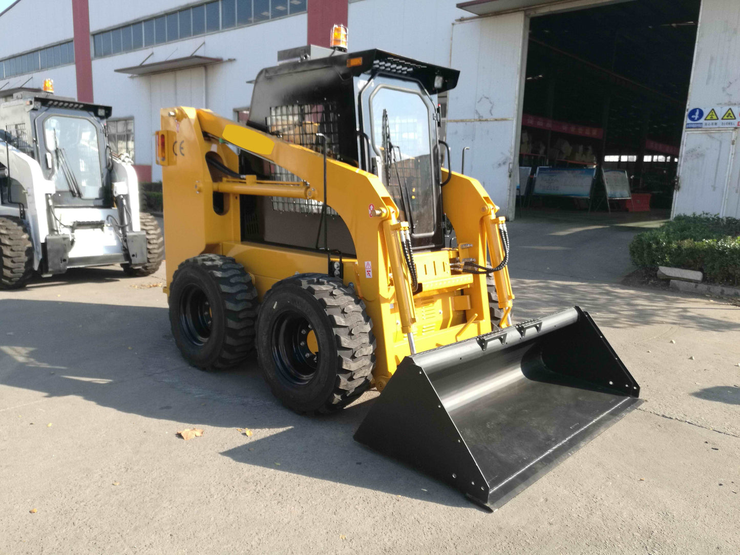 Yellow wheeled skid steer loader parked outside a factory in Canada showing front bucket and durable wheels for construction and farming work



