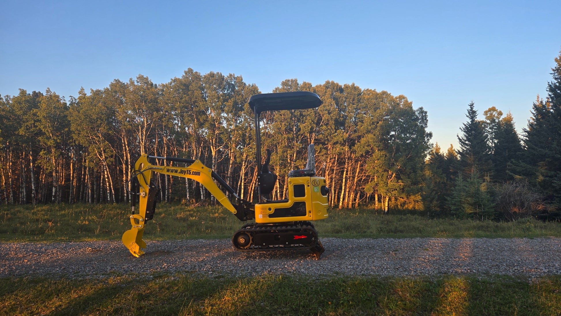 YardHoe YH12 compact yard excavator parked on gravel in front of trees in Canada small digging machine for landscaping and farm work with JoyT5 parts support
