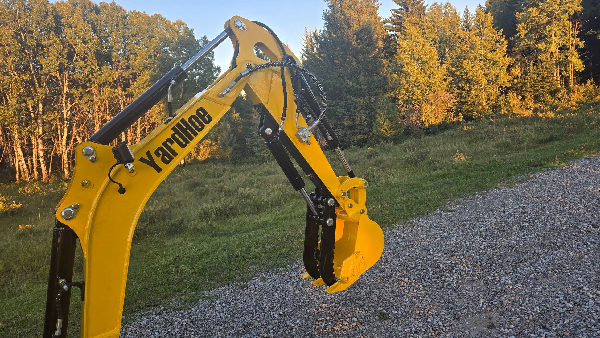 Close-up view of YardHoe YH12 mini excavator arm and digging bucket on gravel path.
