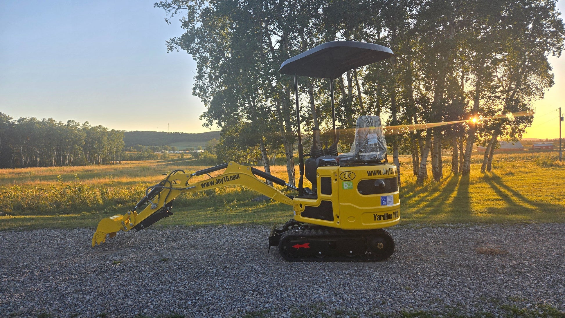 YardHoe YH12 mini excavator with boom arm lowered on gravel road at sunset.
