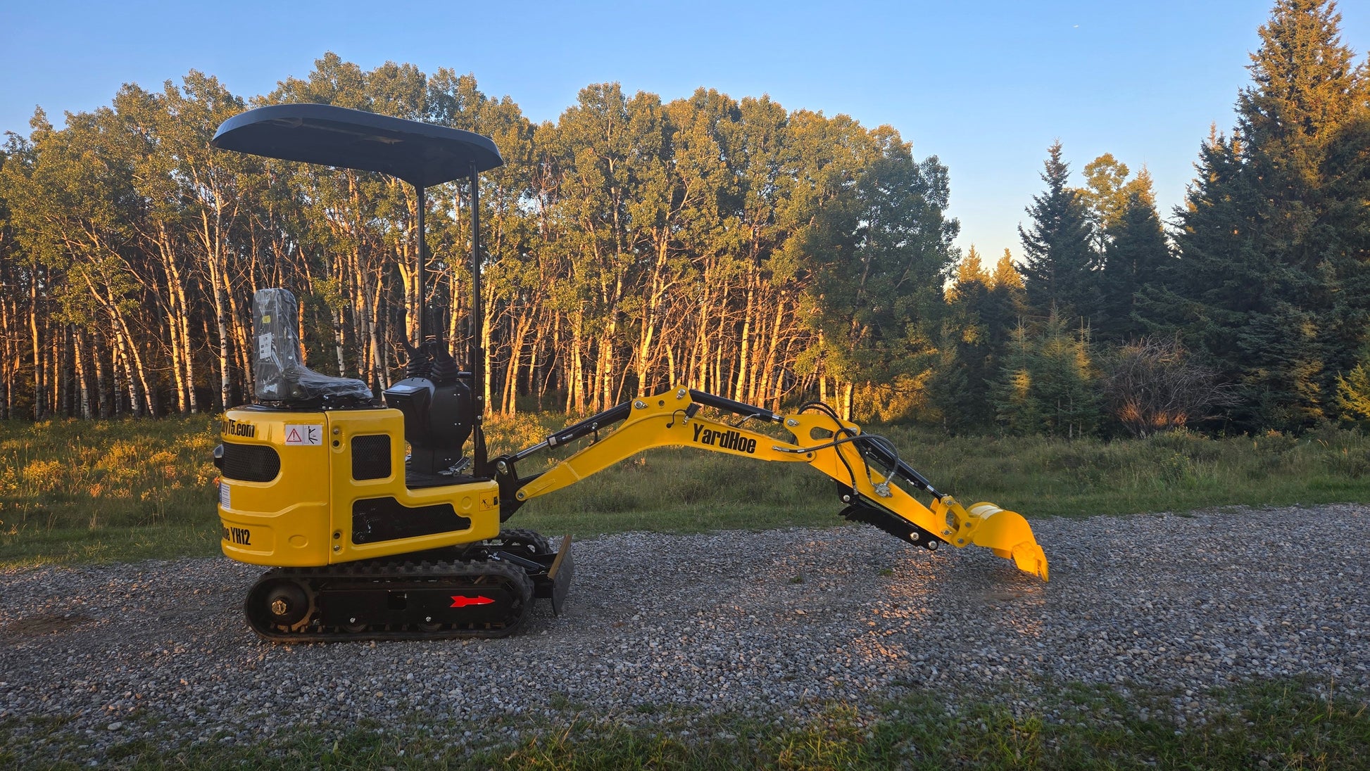 YardHoe YH12 mini excavator with boom and bucket lowered in digging position on gravel road.
