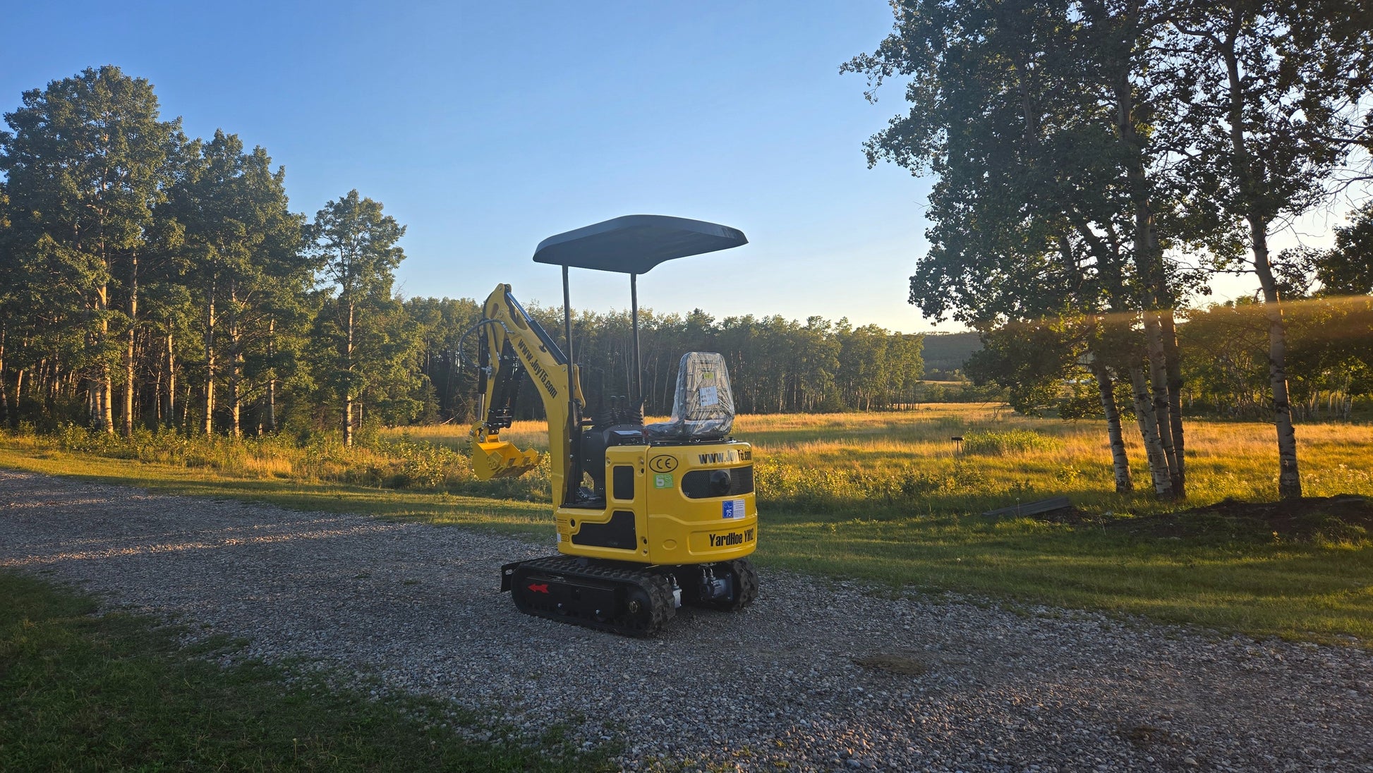 Rear view of YardHoe YH12 mini excavator with canopy, parked on gravel road in a field.
