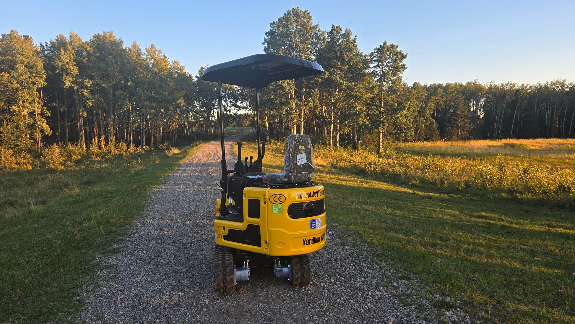 Rear view of YardHoe YH12 mini excavator parked on a gravel road with trees in the background.
