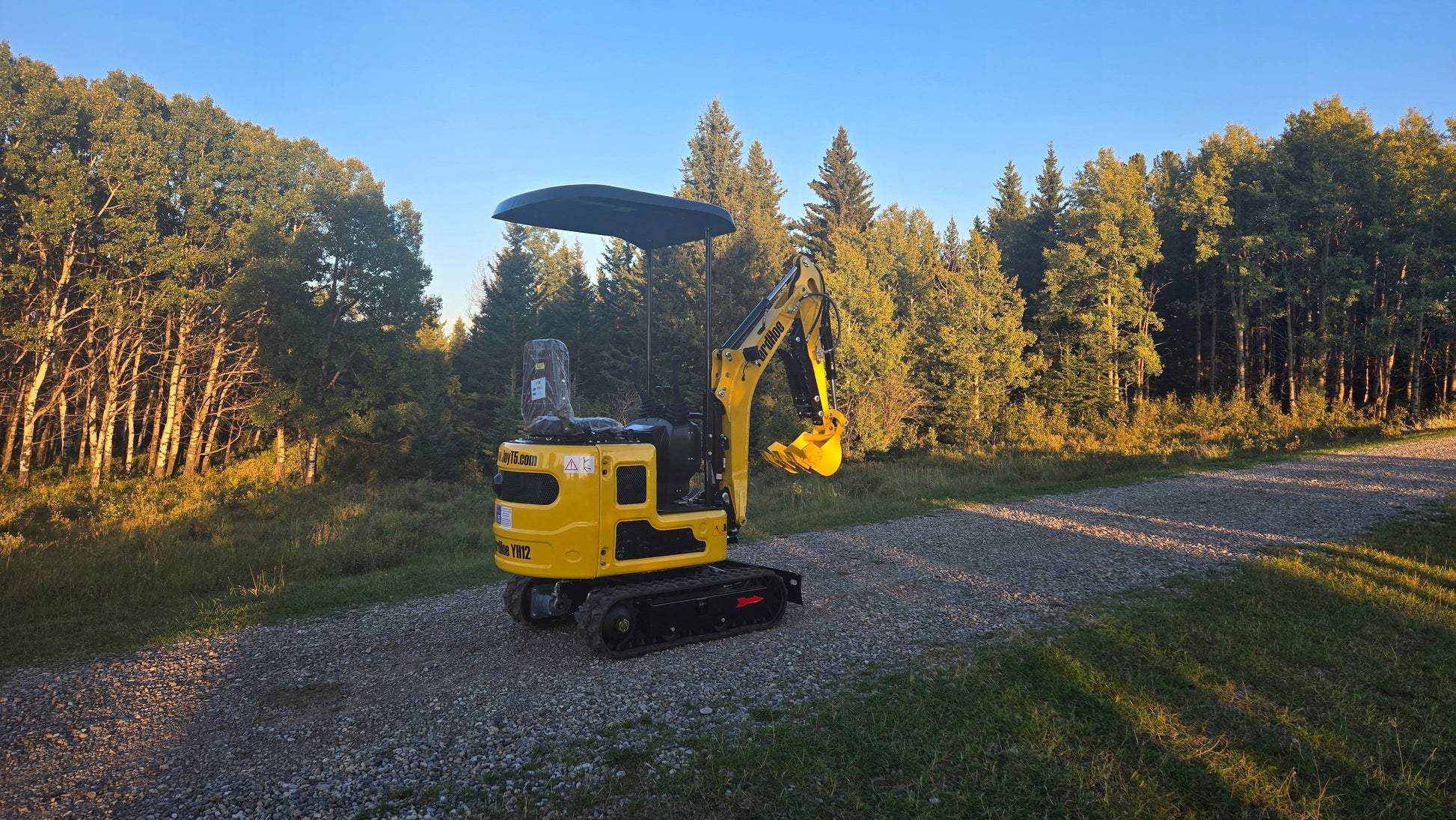 Side-rear view of YardHoe YH12 mini excavator parked on gravel road with trees in the background.
