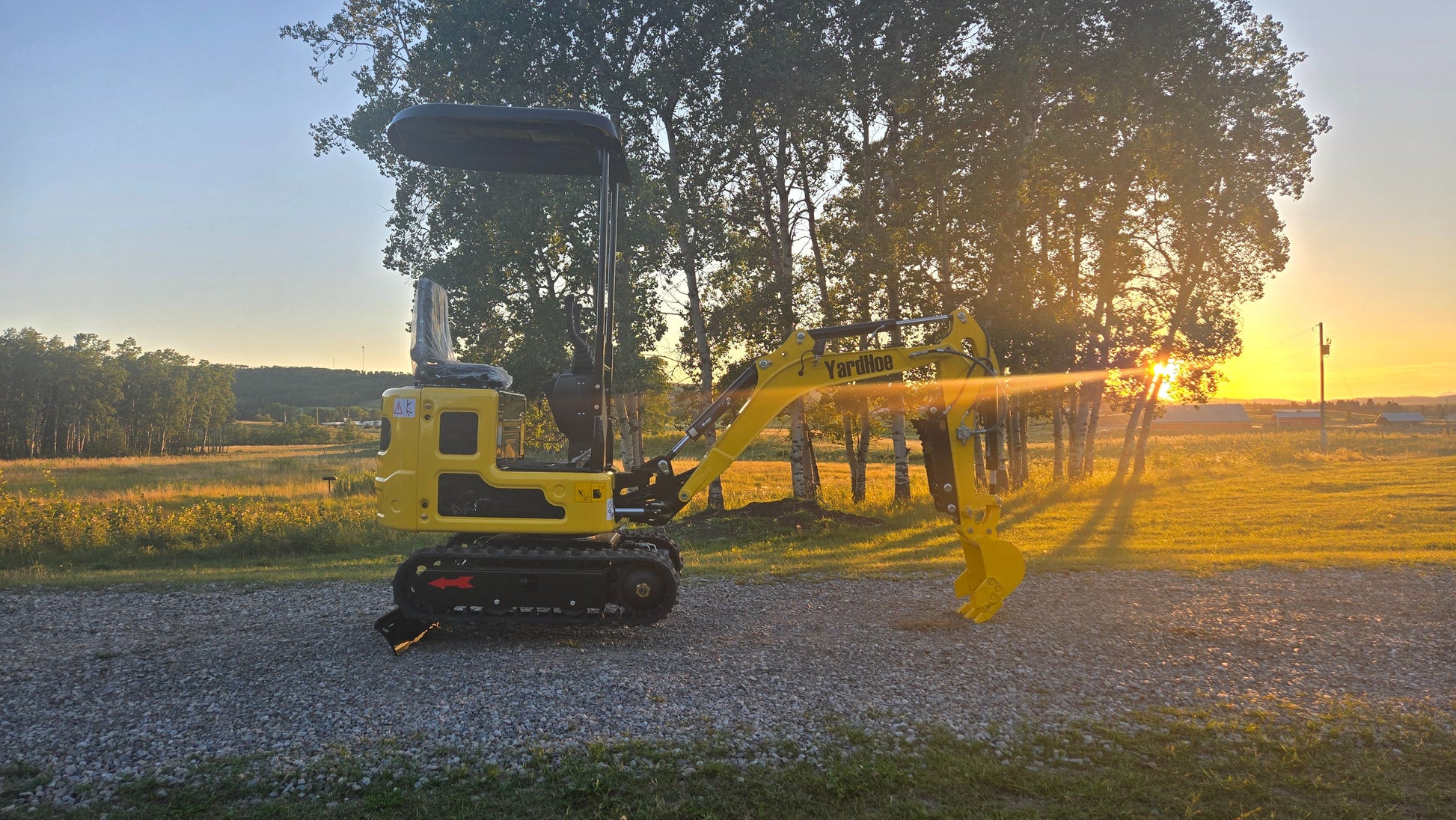 YardHoe YH12 mini excavator side view with digging arm extended at sunset in a rural field.
