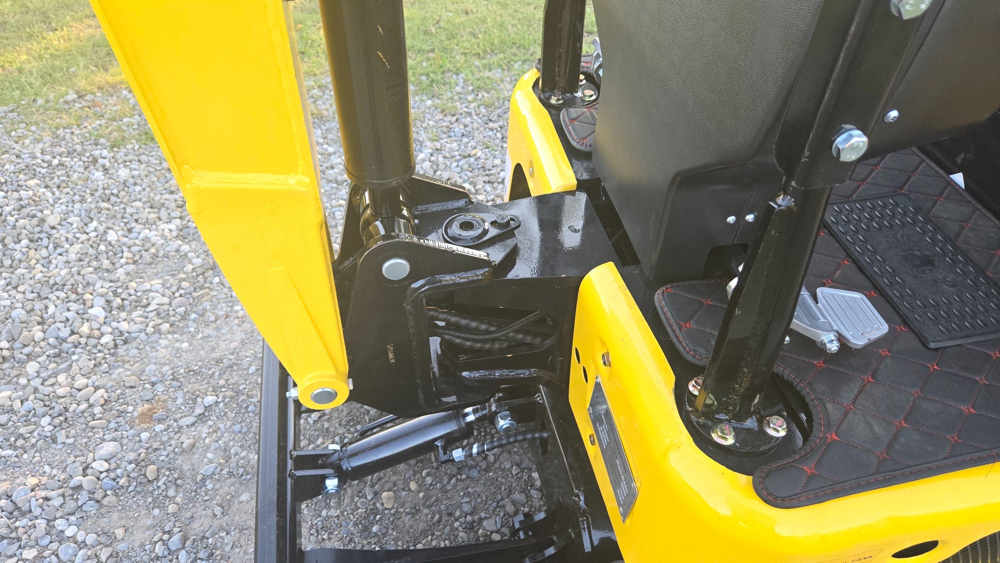Detailed view of YardHoe YH12 / Rippa R319 mini excavator boom base, hydraulic lines, and operator foot pedals.
