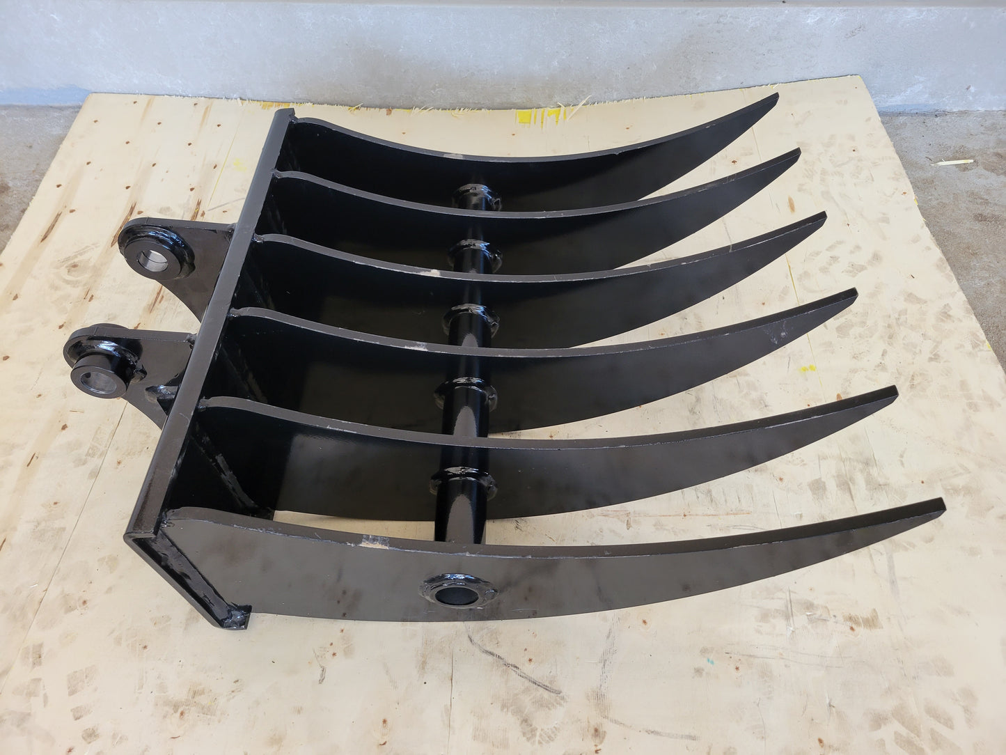 Mini excavator rake attachment side view showing durable curved tines for site cleanup landscaping and debris removal work in Canada