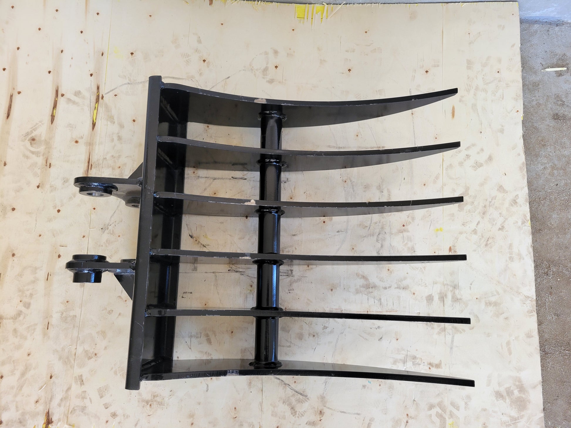 Mini excavator rake attachment top view showing heavy duty curved tines for landscaping site cleanup and debris removal in Canada

